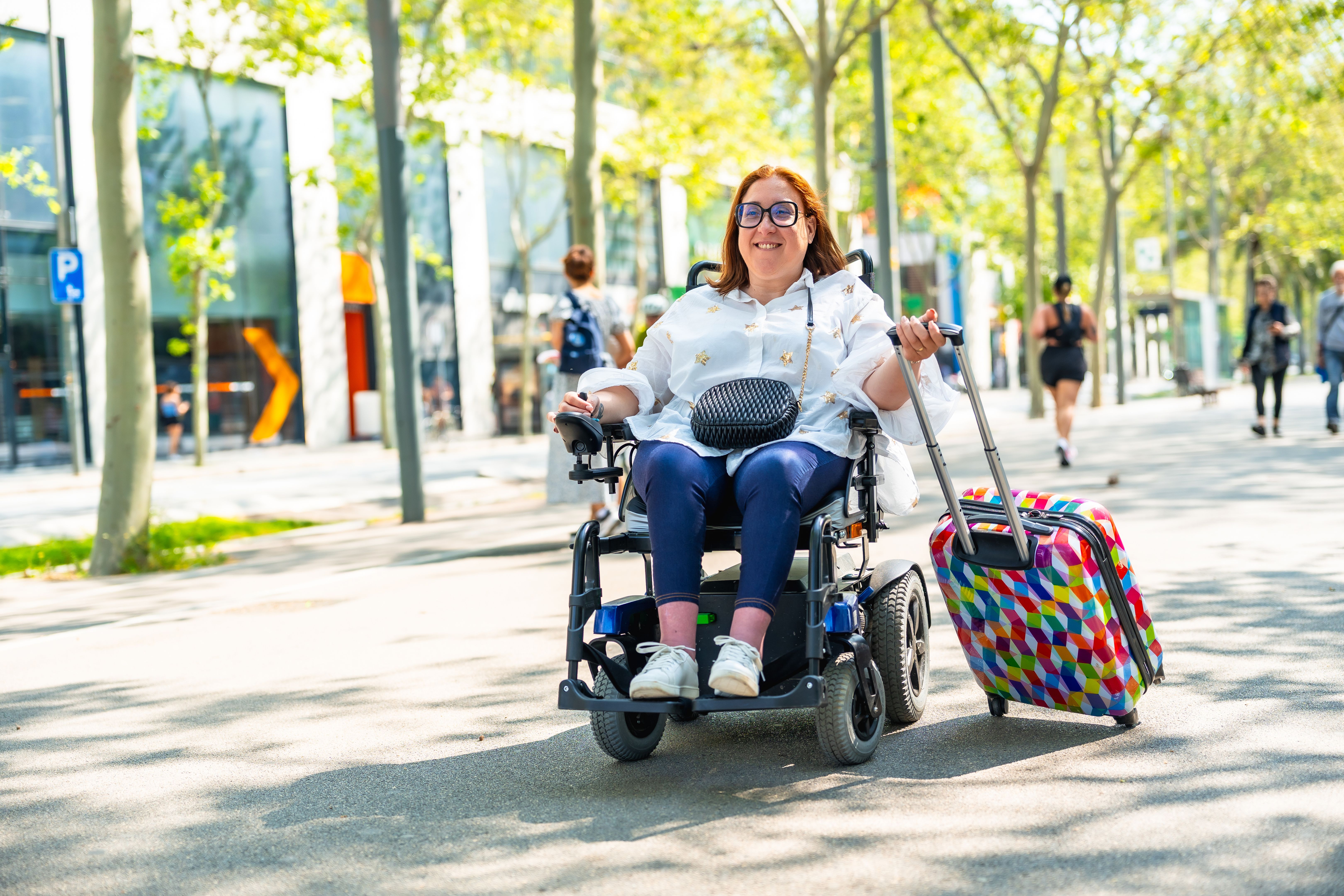 Smiling tourist in wheelchair pulling suitcase enjoying a sunny day