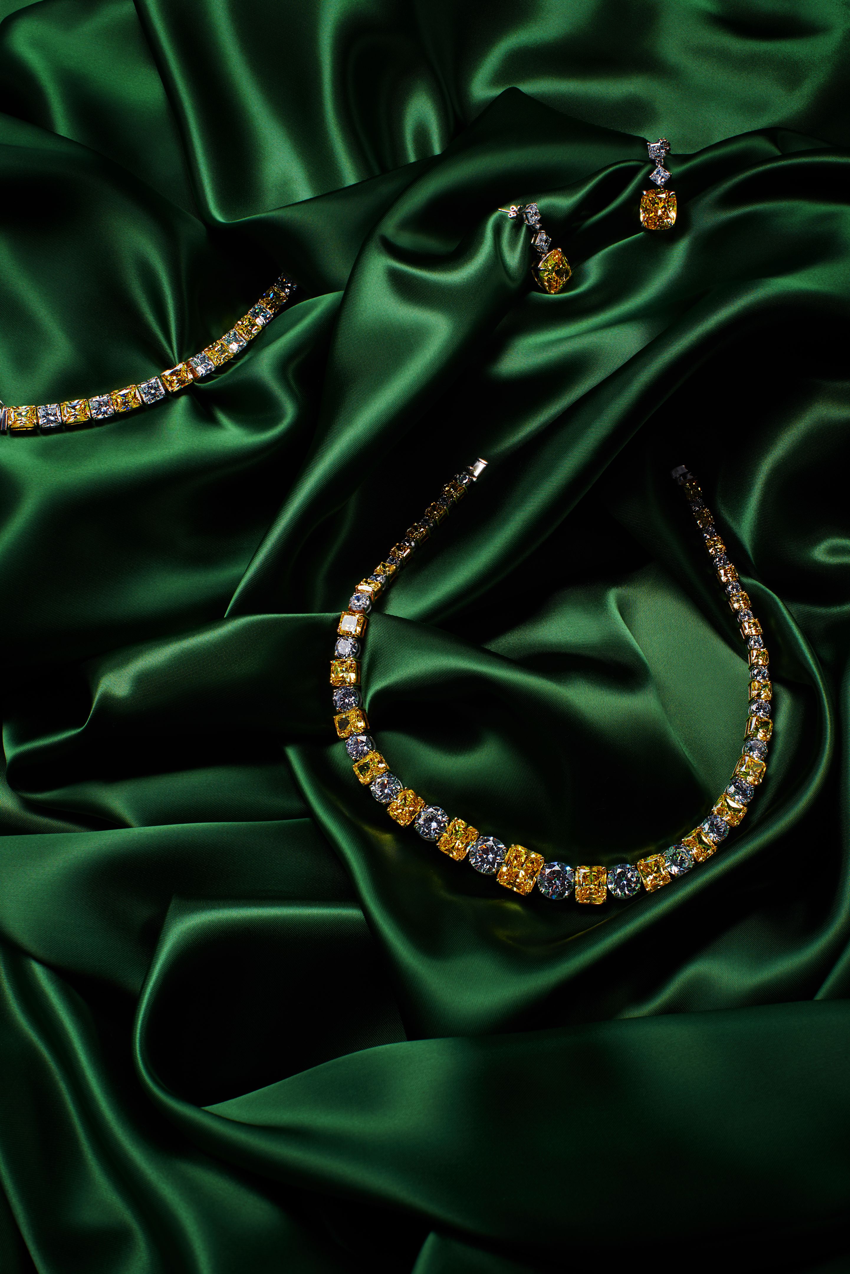 Artistic photography of luxury gold necklace, earrings and bracelet with natural yellow gemstones and diamonds on green silk
