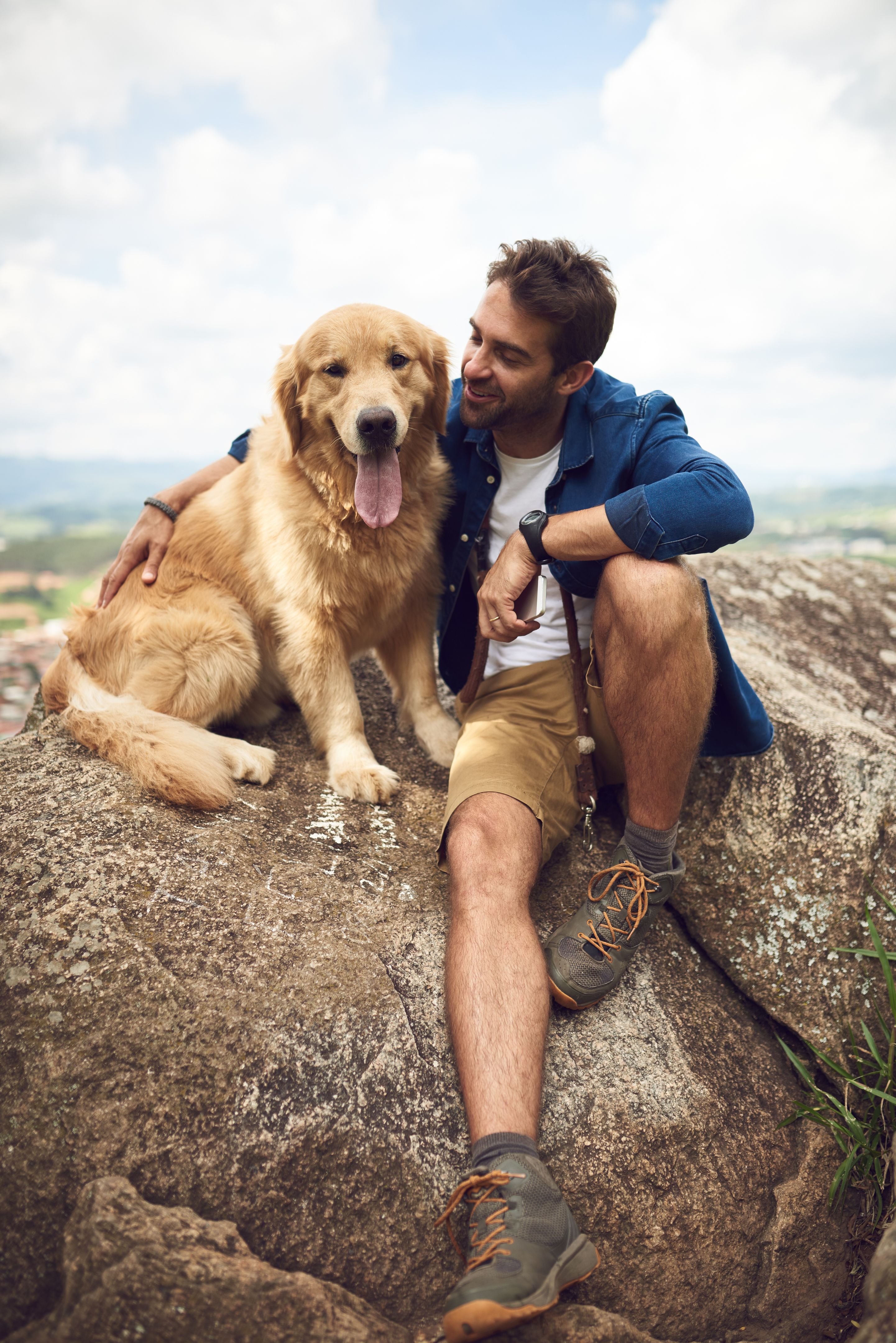 A man sitting on a rock, with his Golden Retriever 