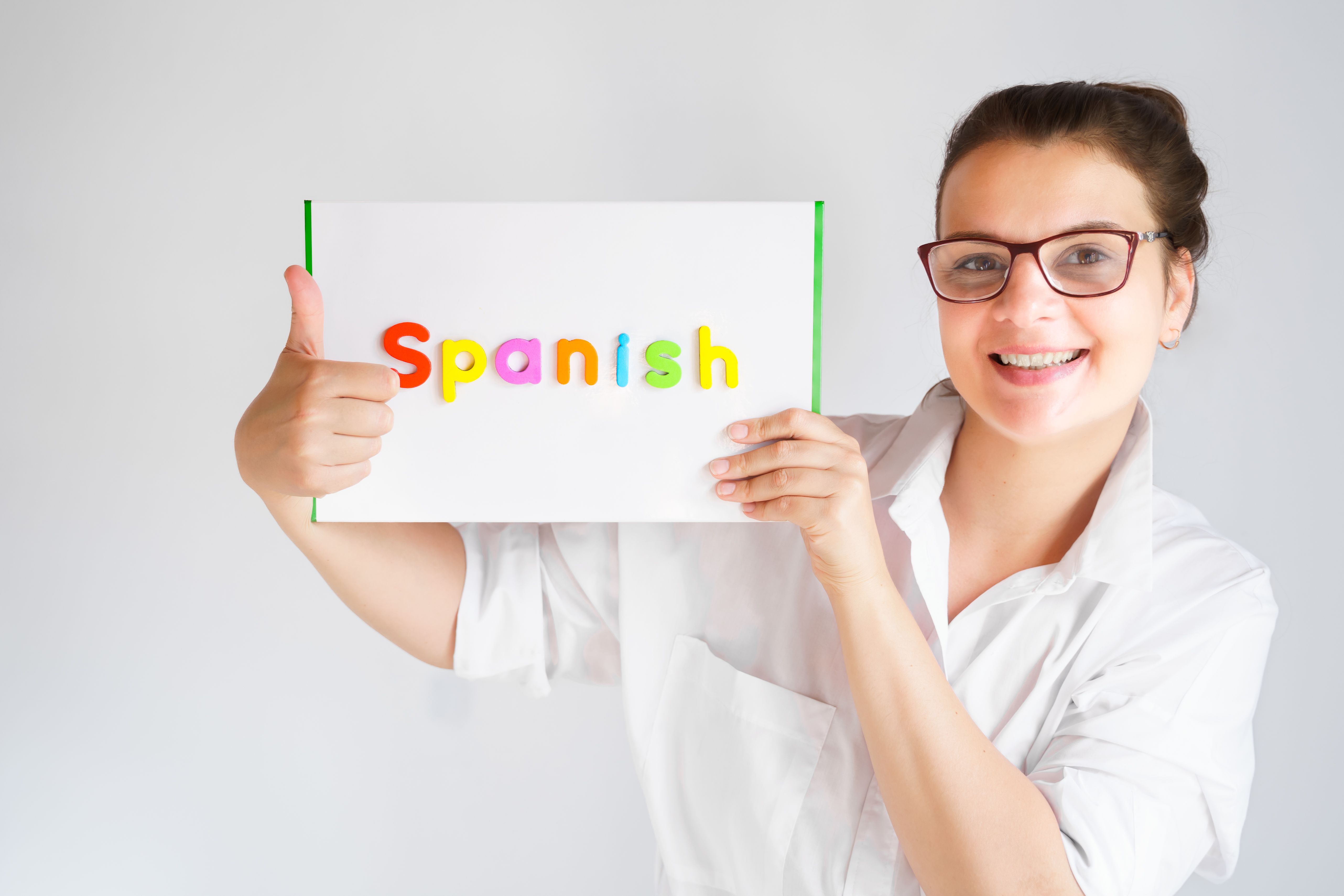 Learning Spanish educational courses. Native tutor, woman teacher in glasses with magnetic sign in hands. Study foreign language in online school. Speaking,reading,writing,linguistic knowledge skills