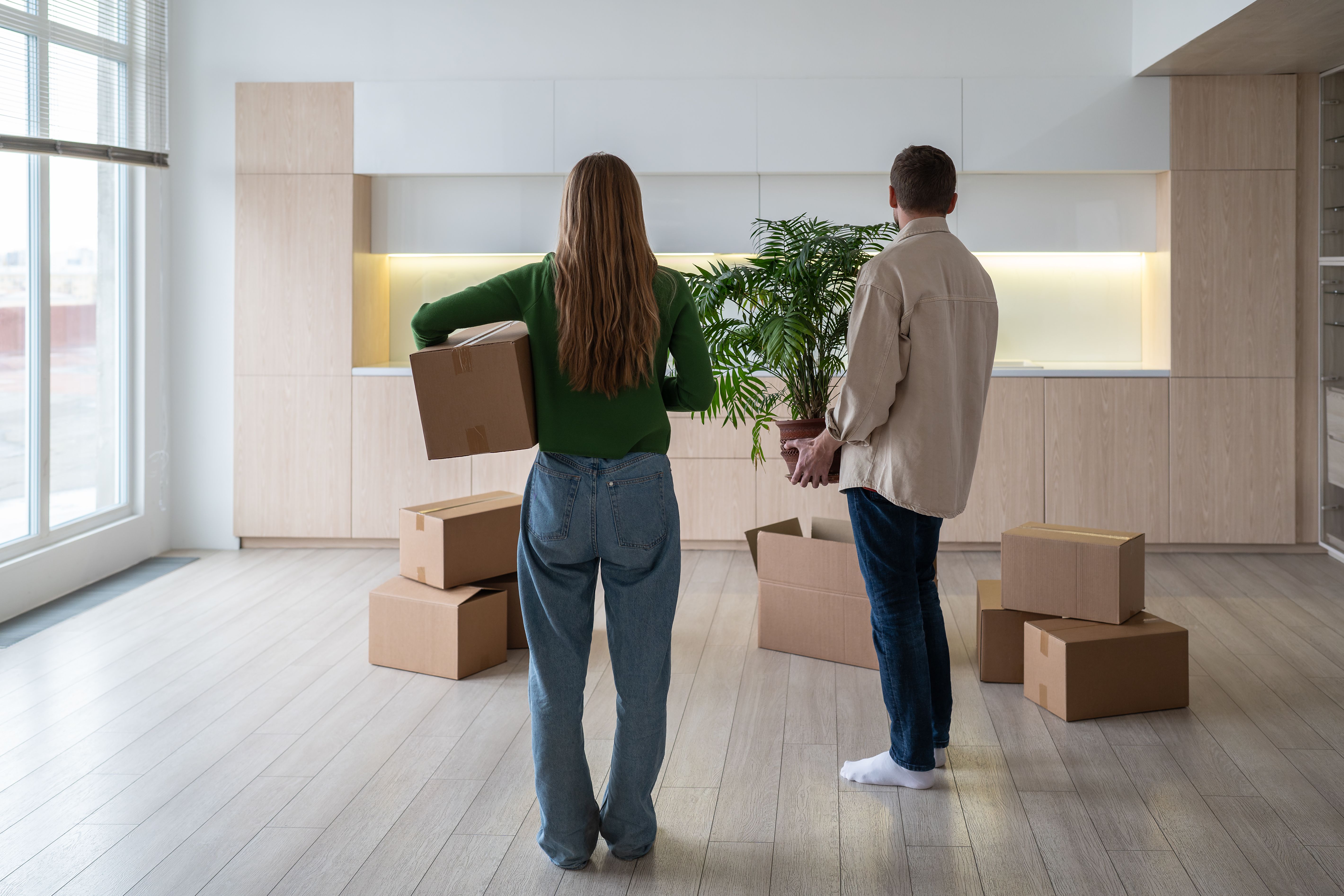 New home owners with boxes and houseplant in hands. Housewarming relocation in mortgage apartment.