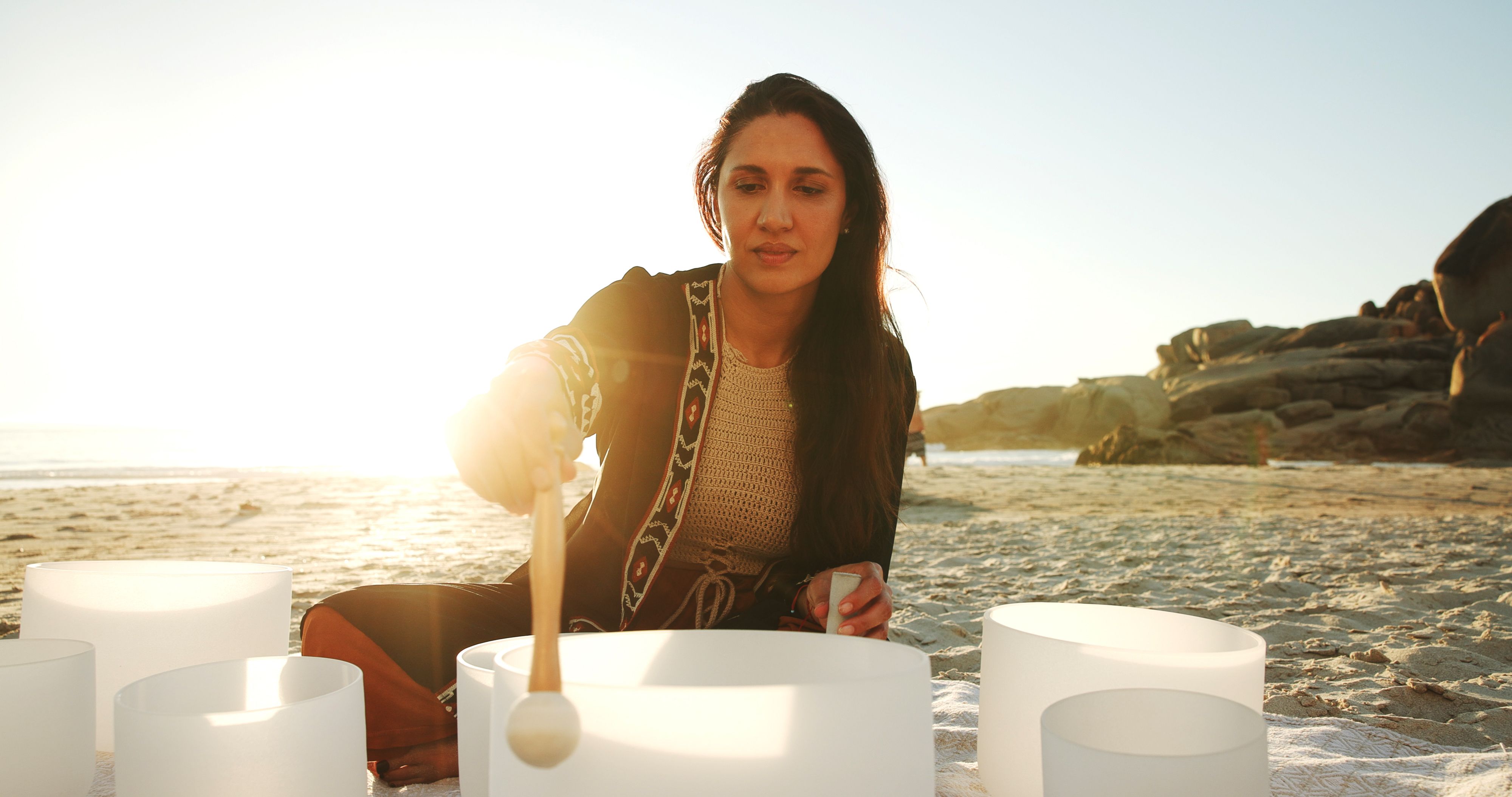 Meditation, sound therapy and woman with bowls at beach for mindfulness, spiritual cleanse and energy. Nature, morning ritual and person with frequency for healing, balance and wellness by ocean
