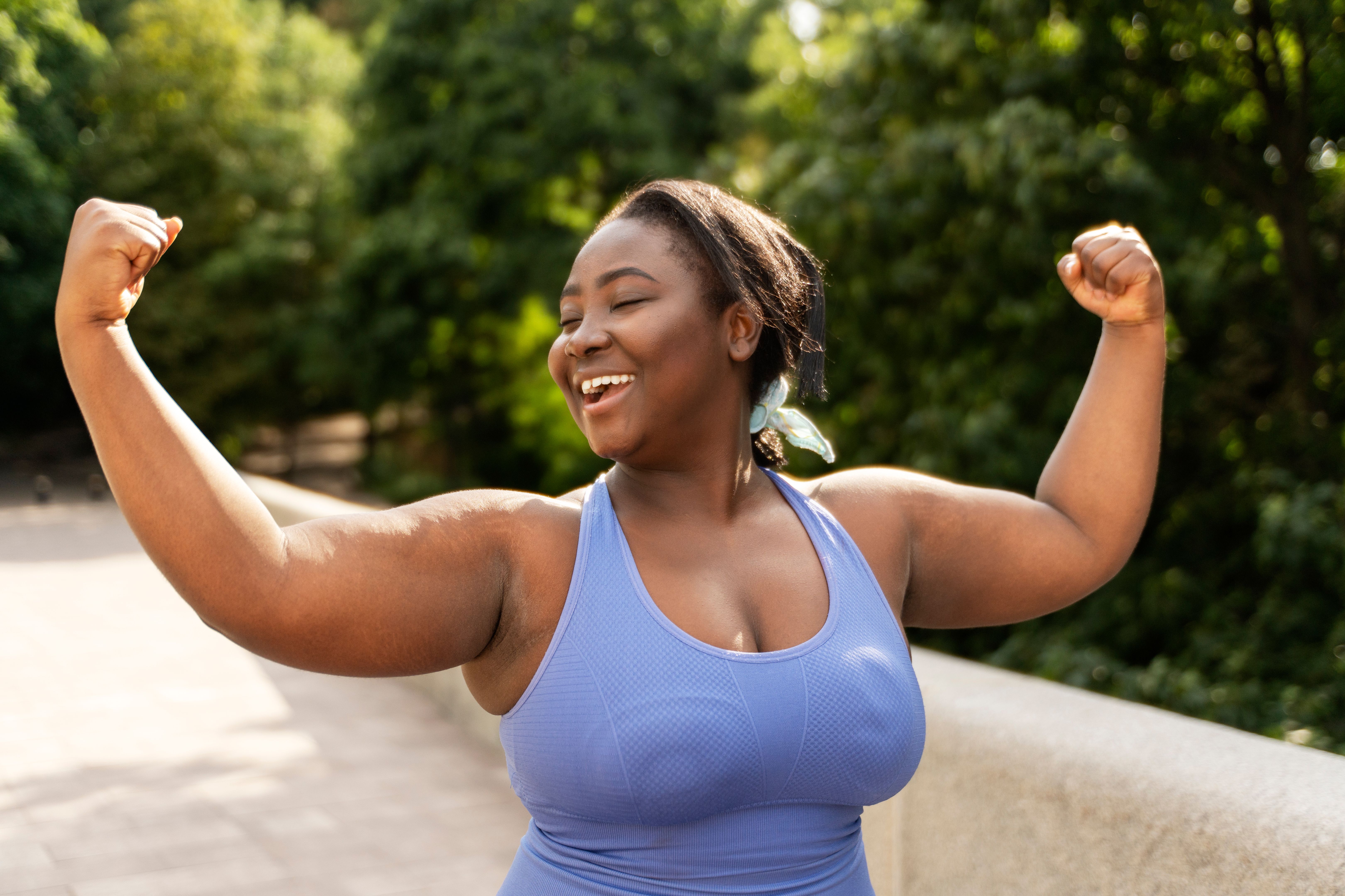 Beautiful smiling African American woman in sportswear showing biceps exercising on the street Beautiful smiling African American woman in sportswear showing biceps exercising on the street