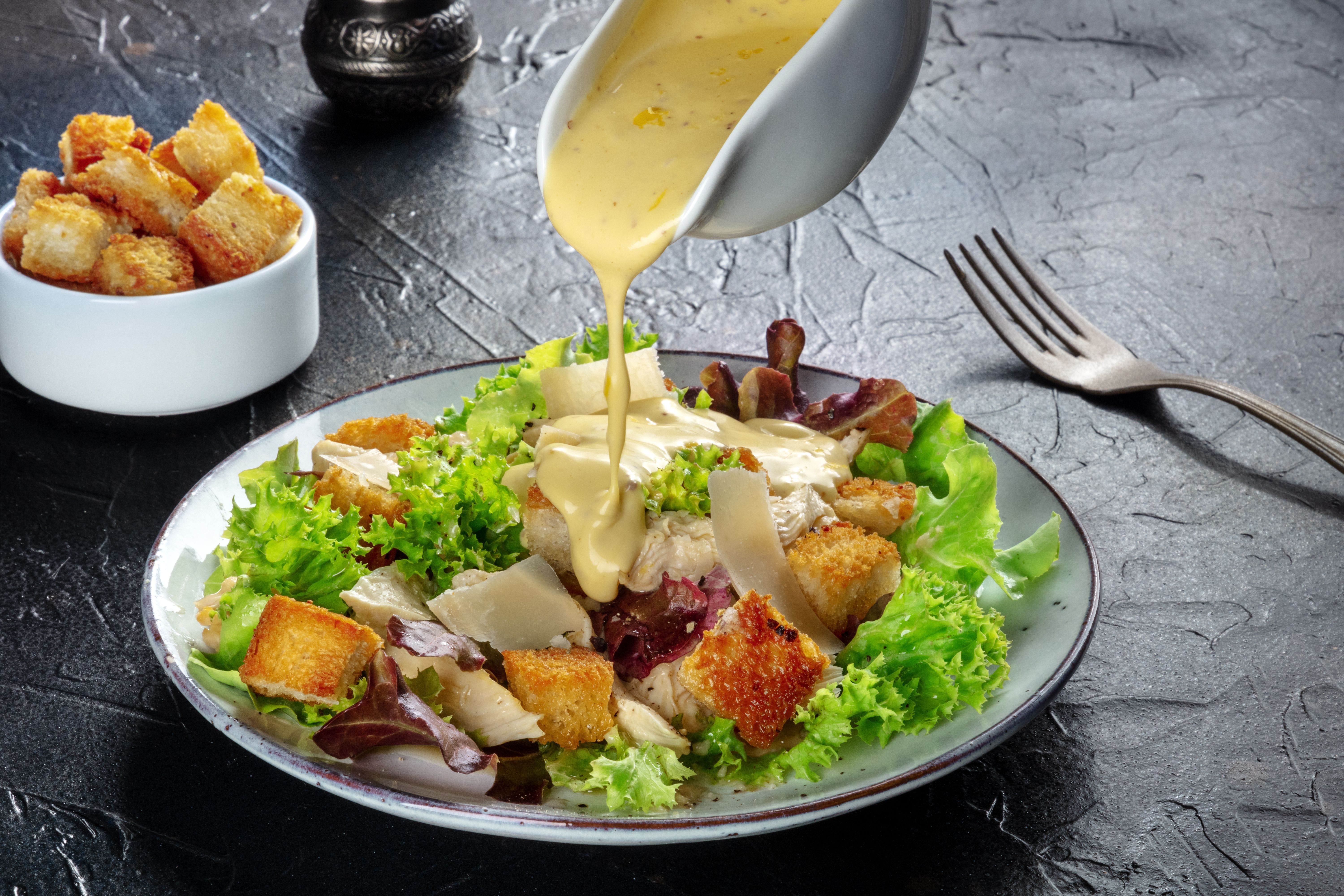 Chicken Caesar salad with the classic dressing being poured and croutons