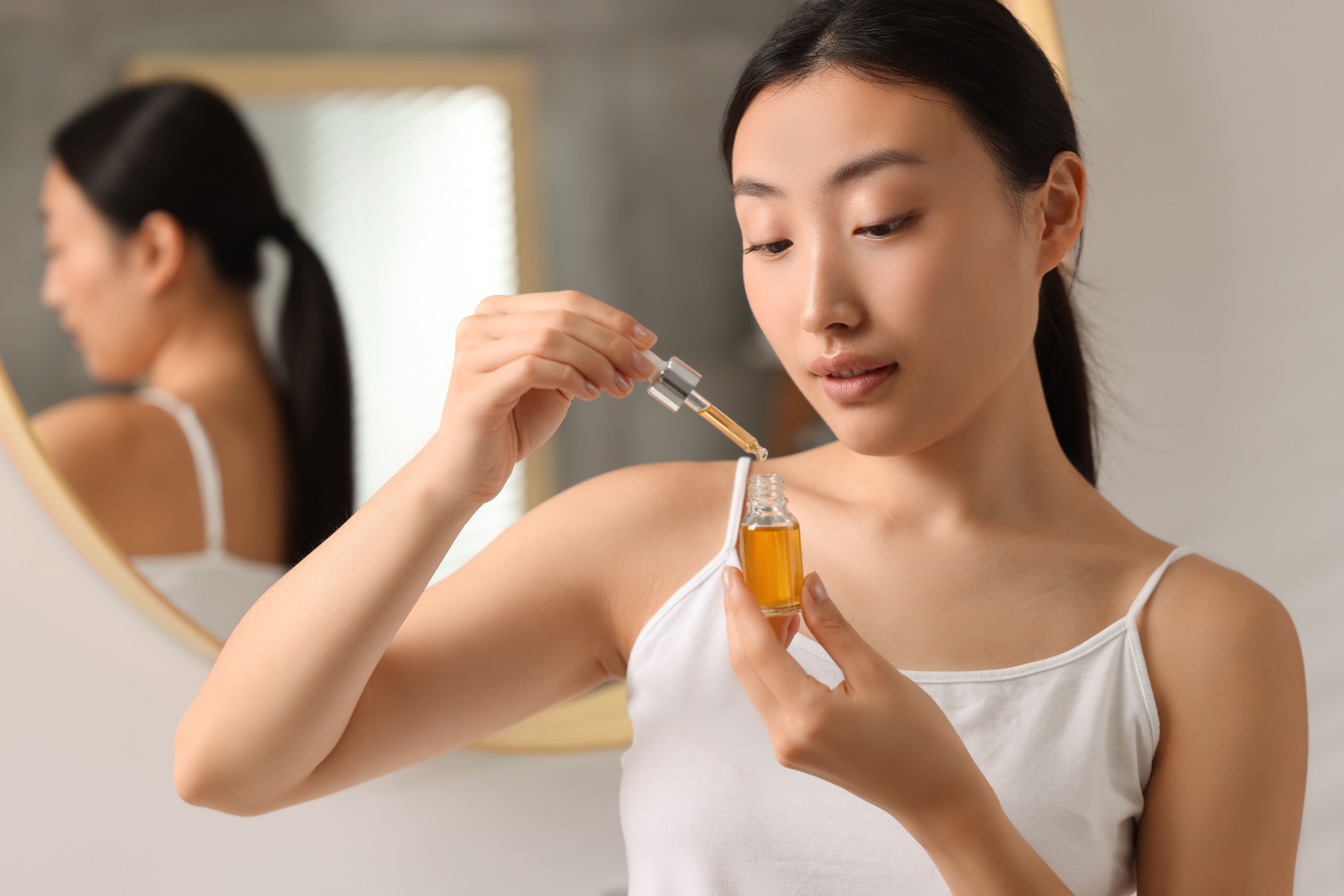 Beautiful young woman with bottle of cosmetic serum in bathroom