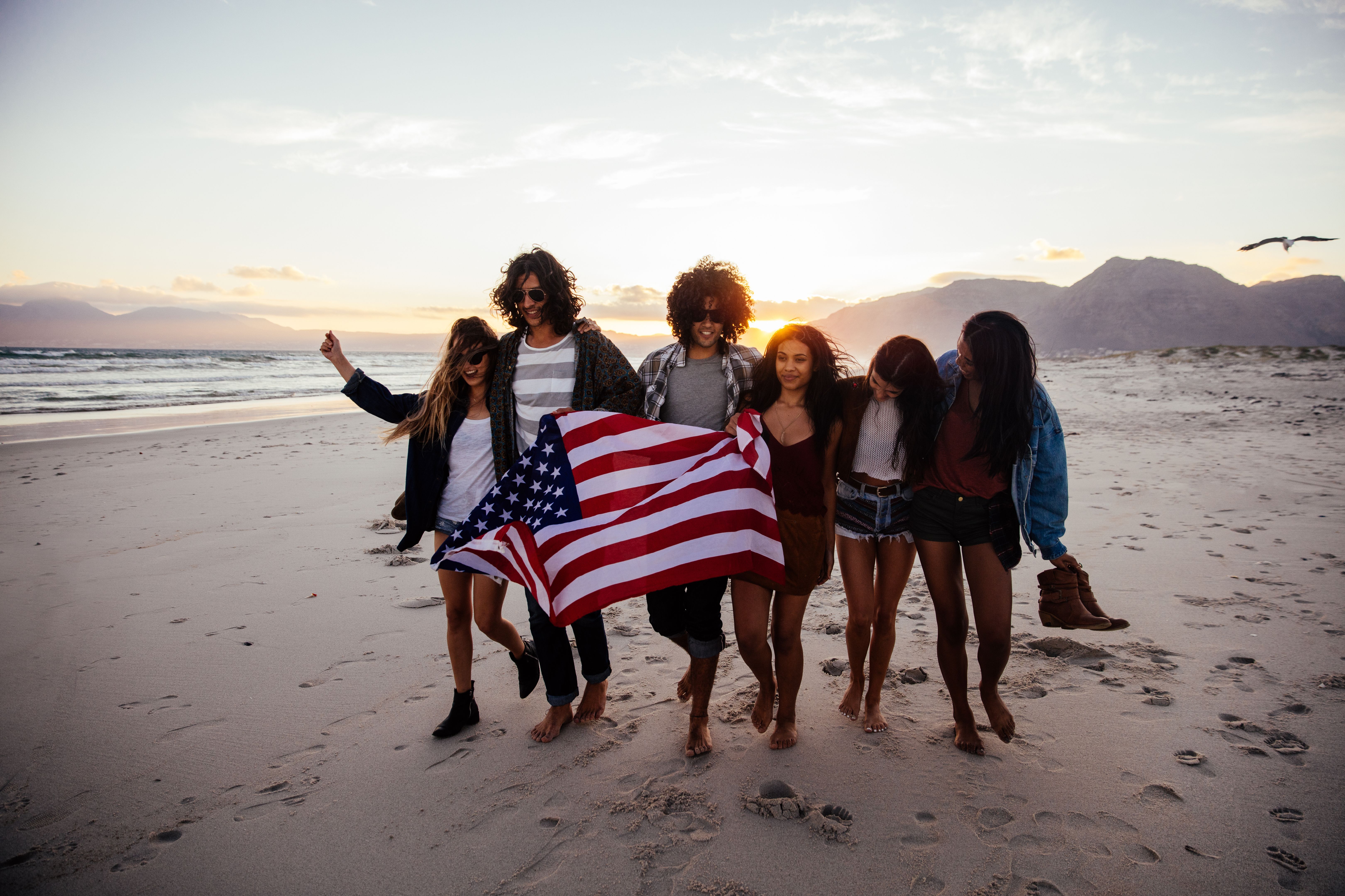Hipster friends walking on the beach holding an American flag