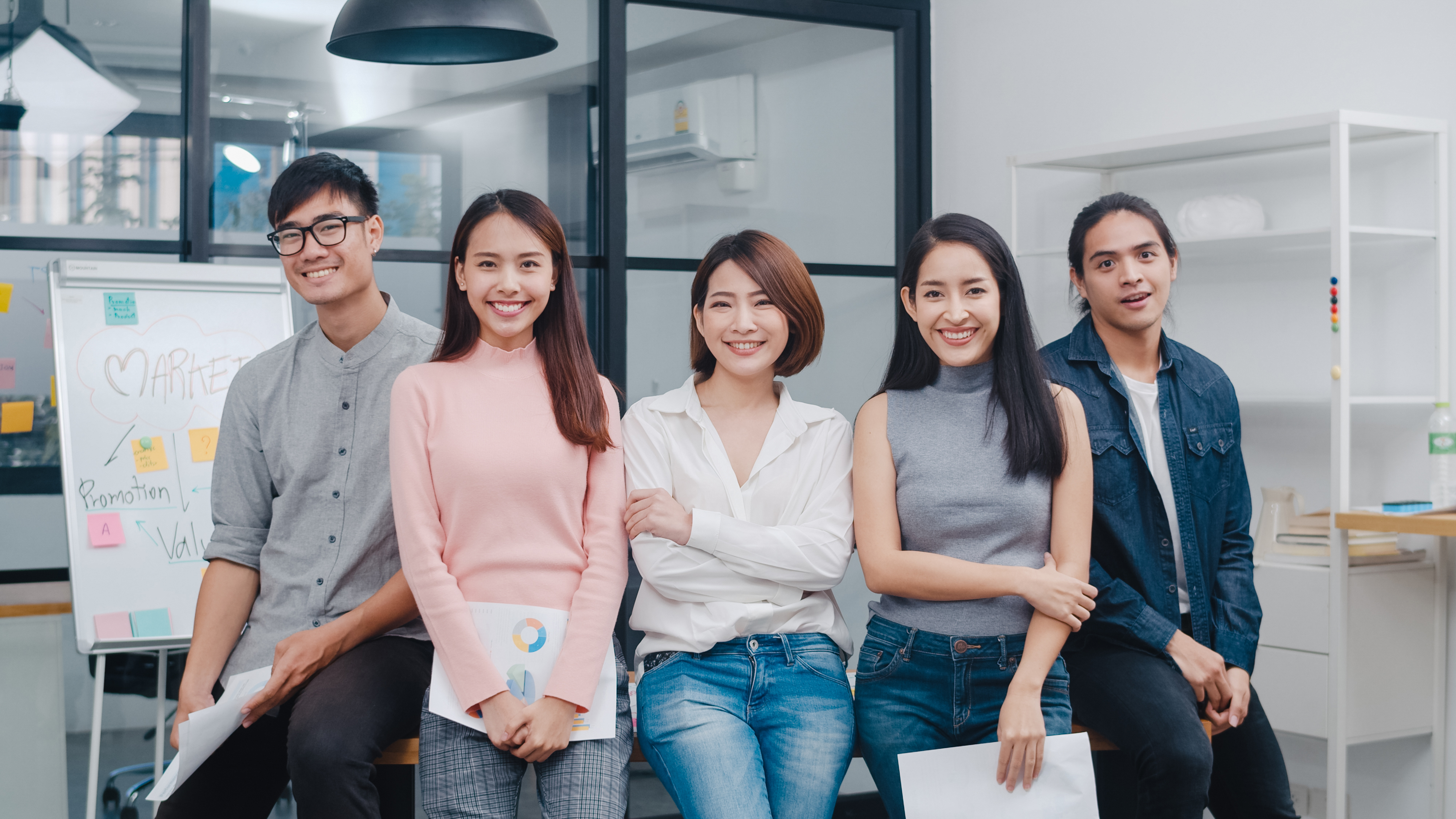 Group of Asia young creative people in smart casual wear looking at camera and smiling in creative office workplace.