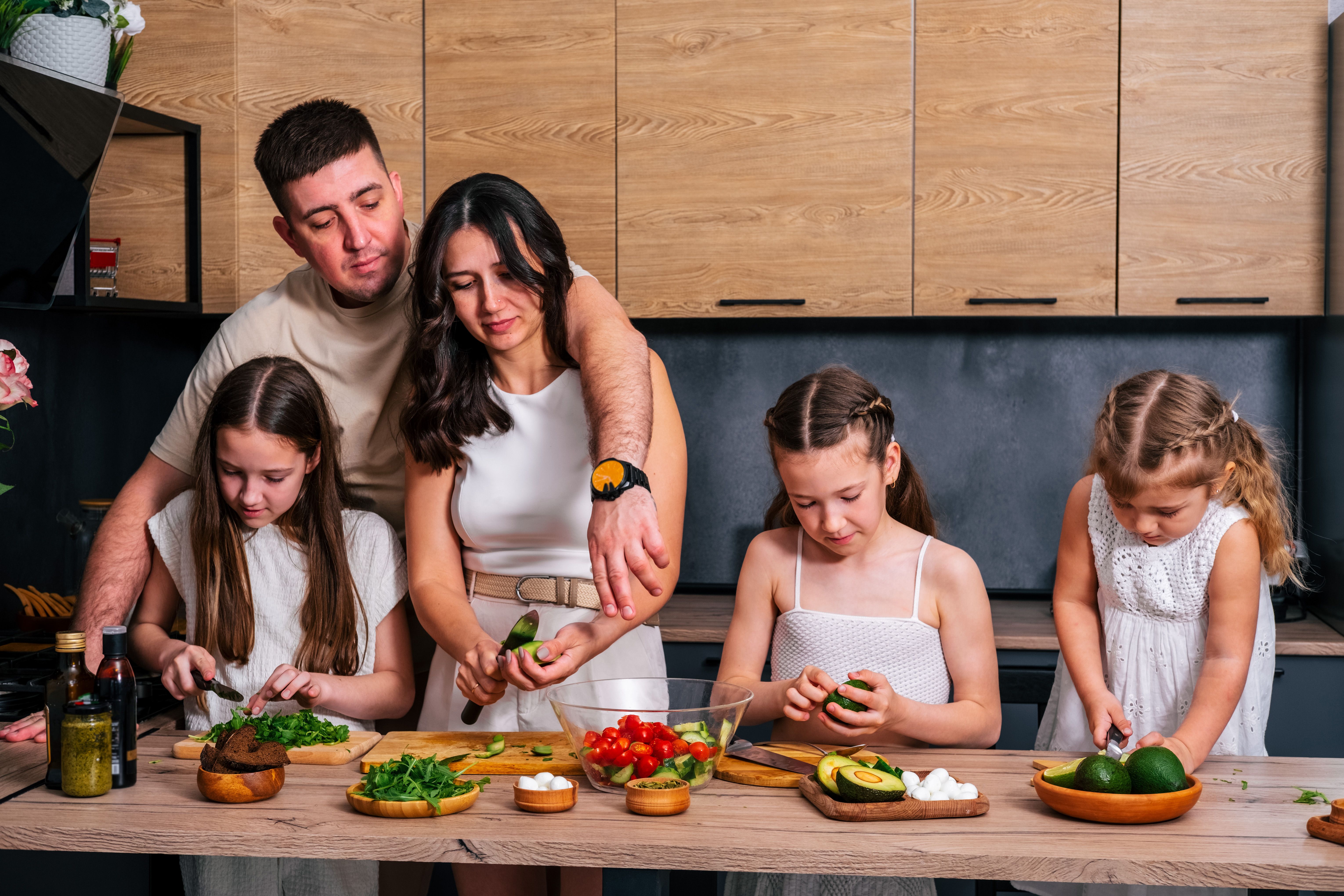 Young parents teach their little daughters to cook  at the kitchen.