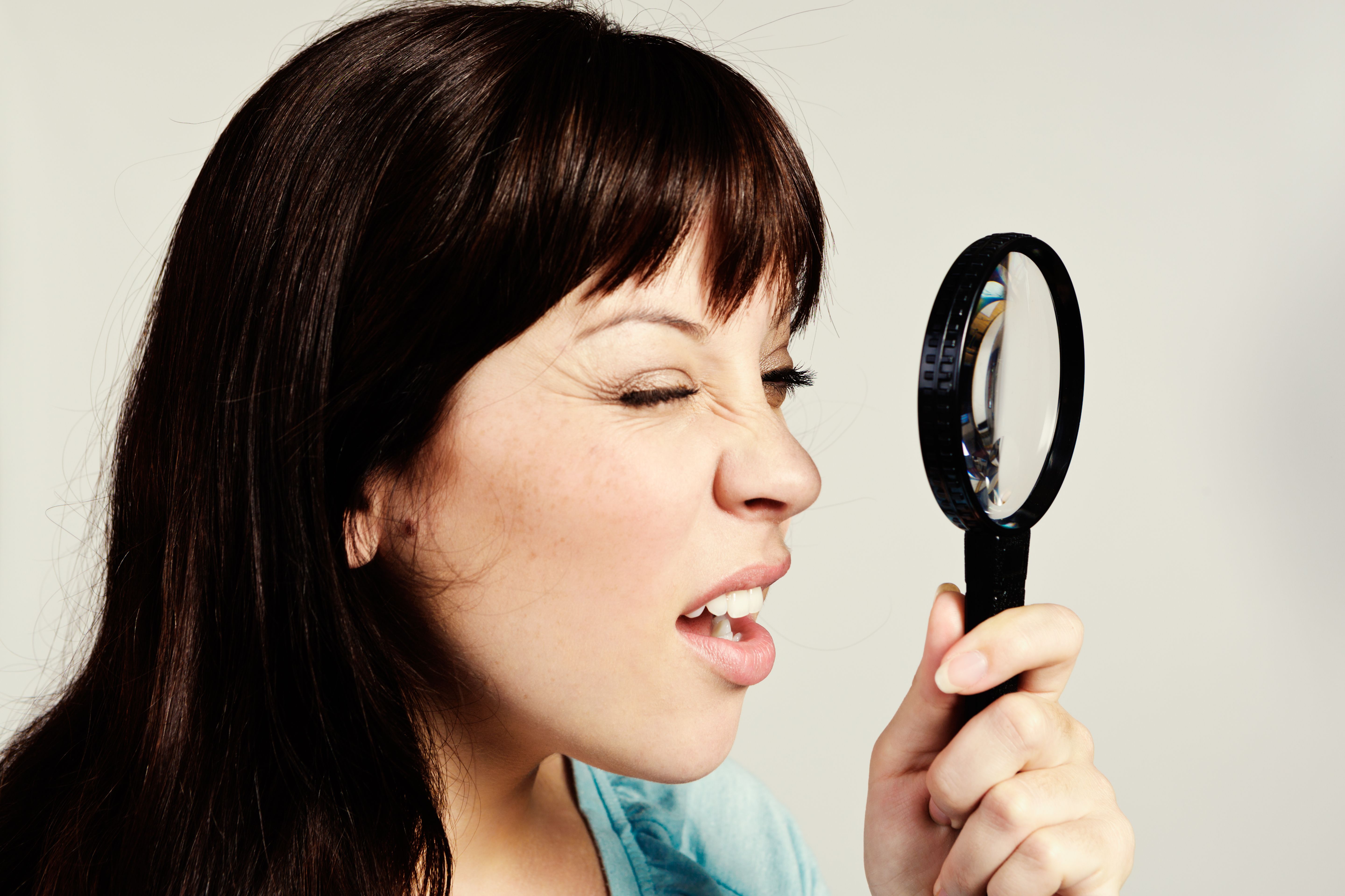 Time for optometrist visit! Pretty brunette squints through magnifying glass