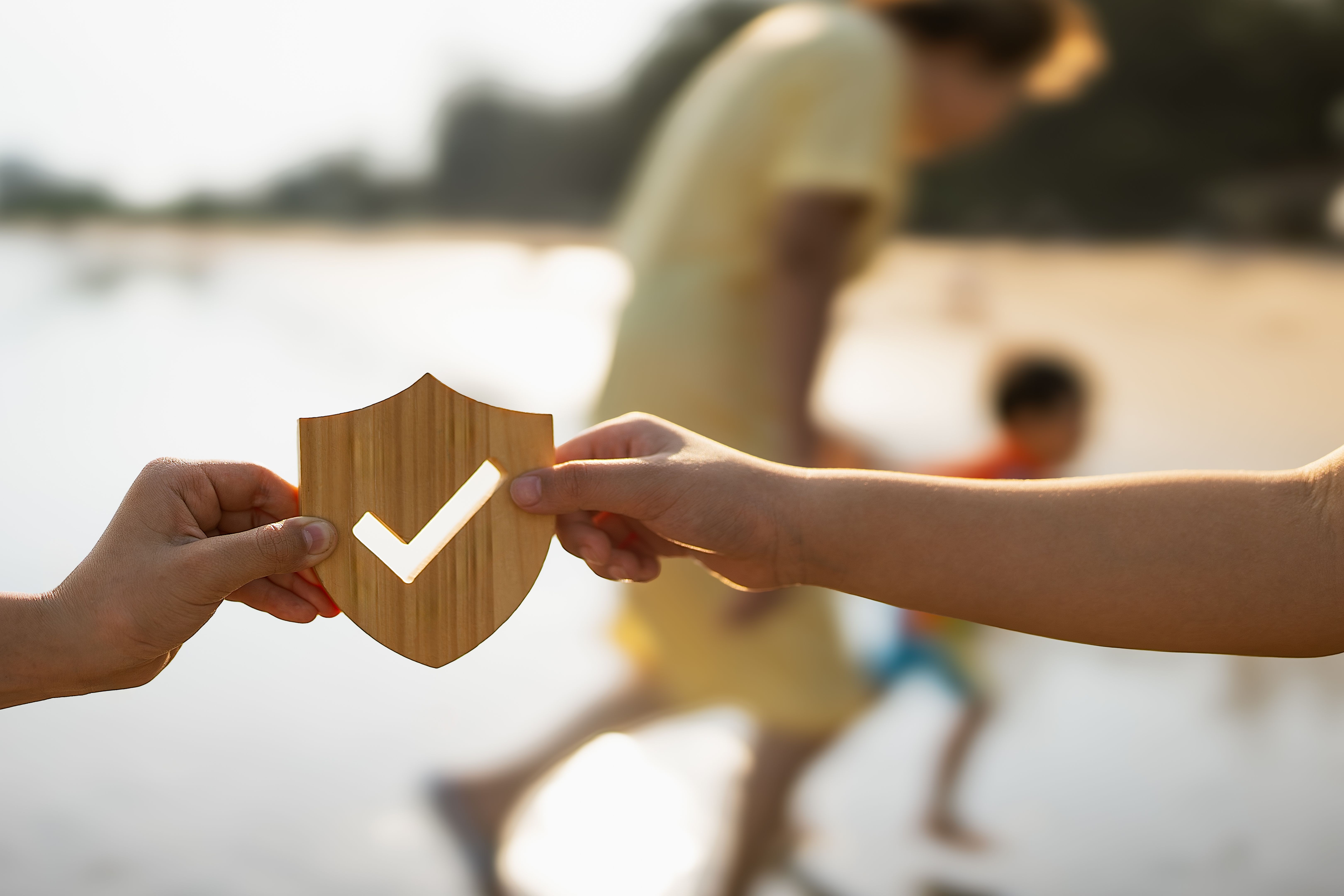 Image of two children's hands holding an insurance model in the shape of a shield with a check mark.