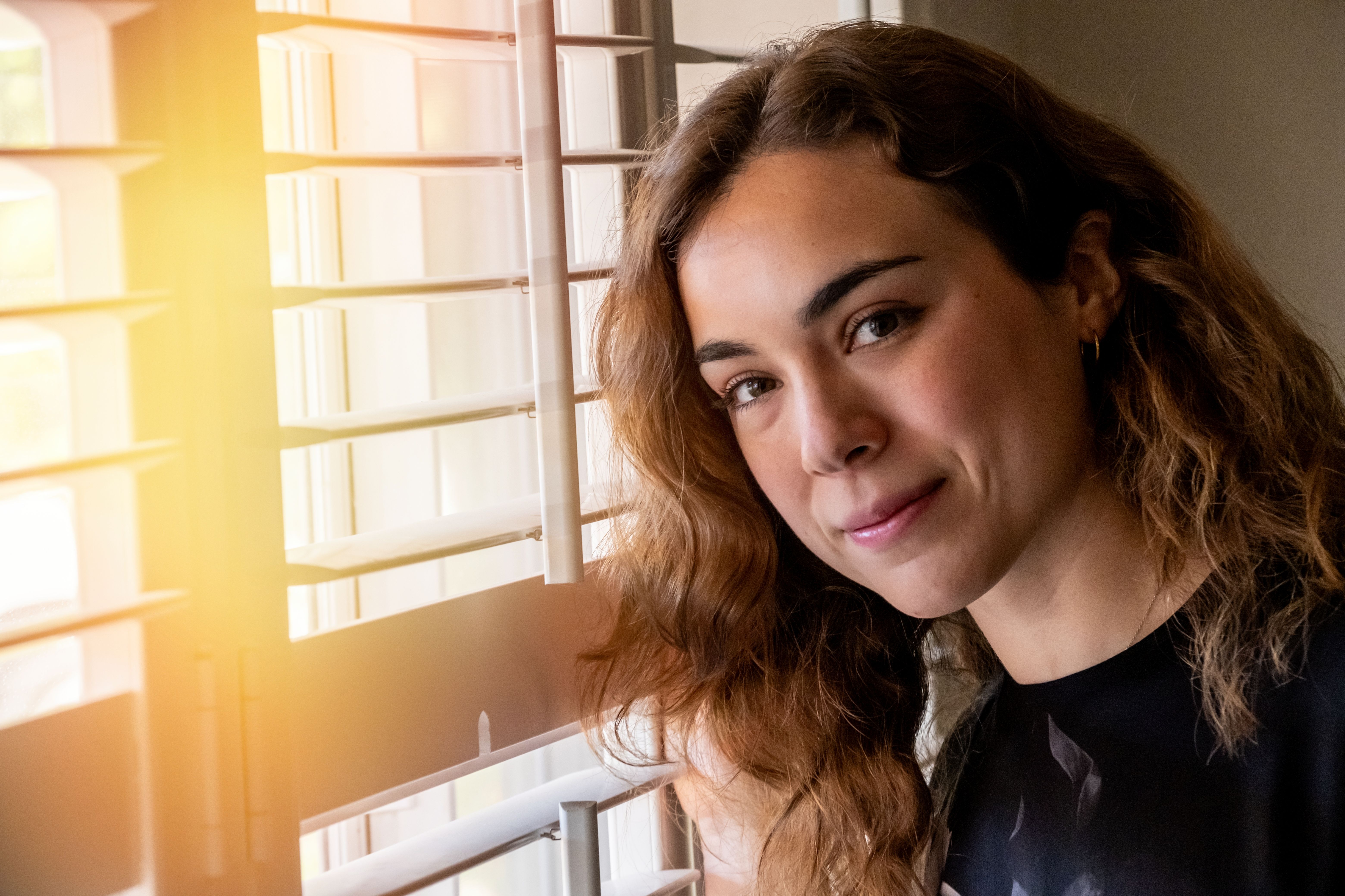 Mulher jovem sorridente olhando para a câmera perto de sua janela de casa