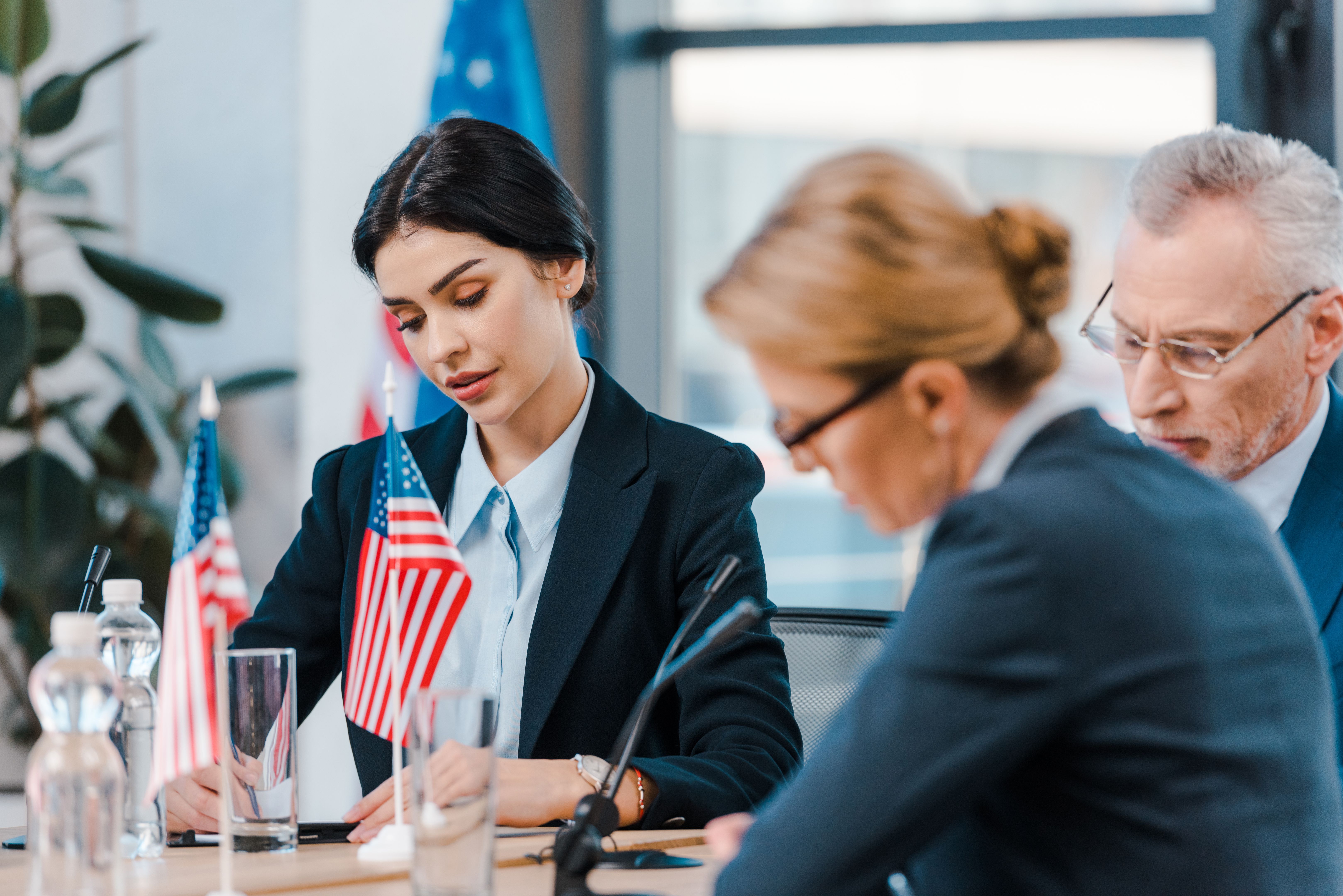 selective focus of attractive businesswoman near diplomats and flags of america