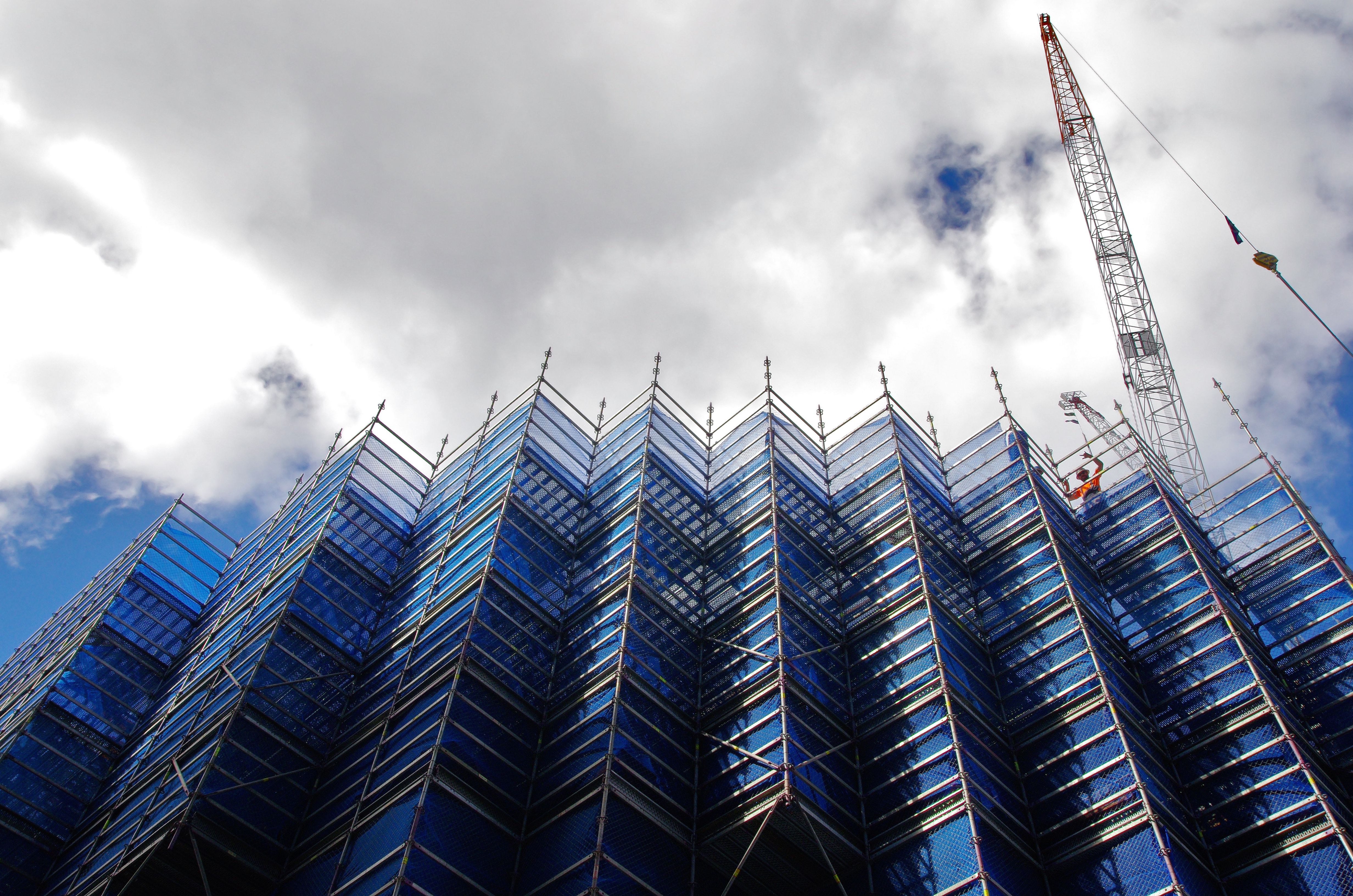 Scaffolding on building. Worker and a crane in the background. Scaffolding on building. Worker and a crane in the background.