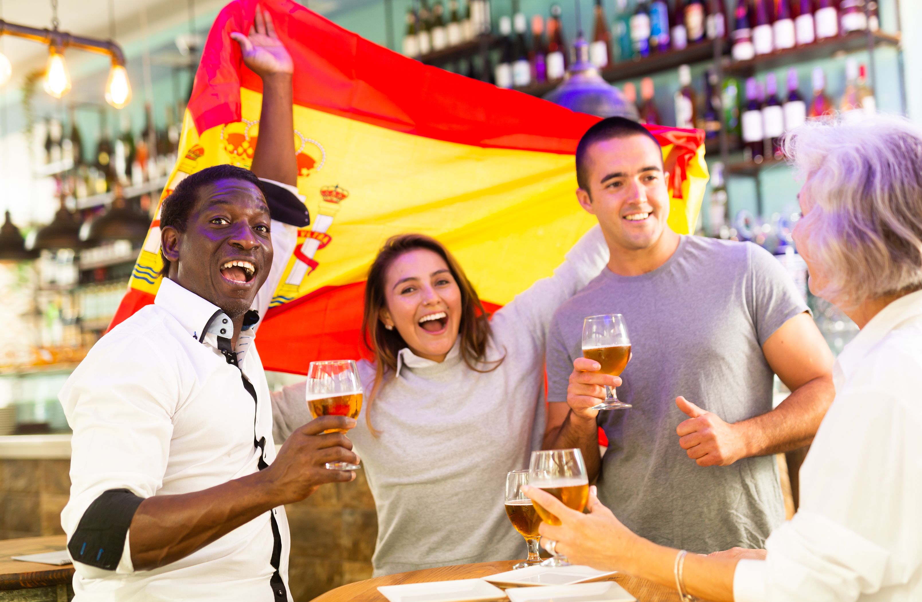 Les fans de football espagnols masculins et féminins célèbrent la victoire du championnat, agitant le drapeau de l’Espagne dans un pub Les fans de football espagnols masculins et féminins célèbrent la victoire du championnat, agitant le drapeau de l’Espagne dans un pub