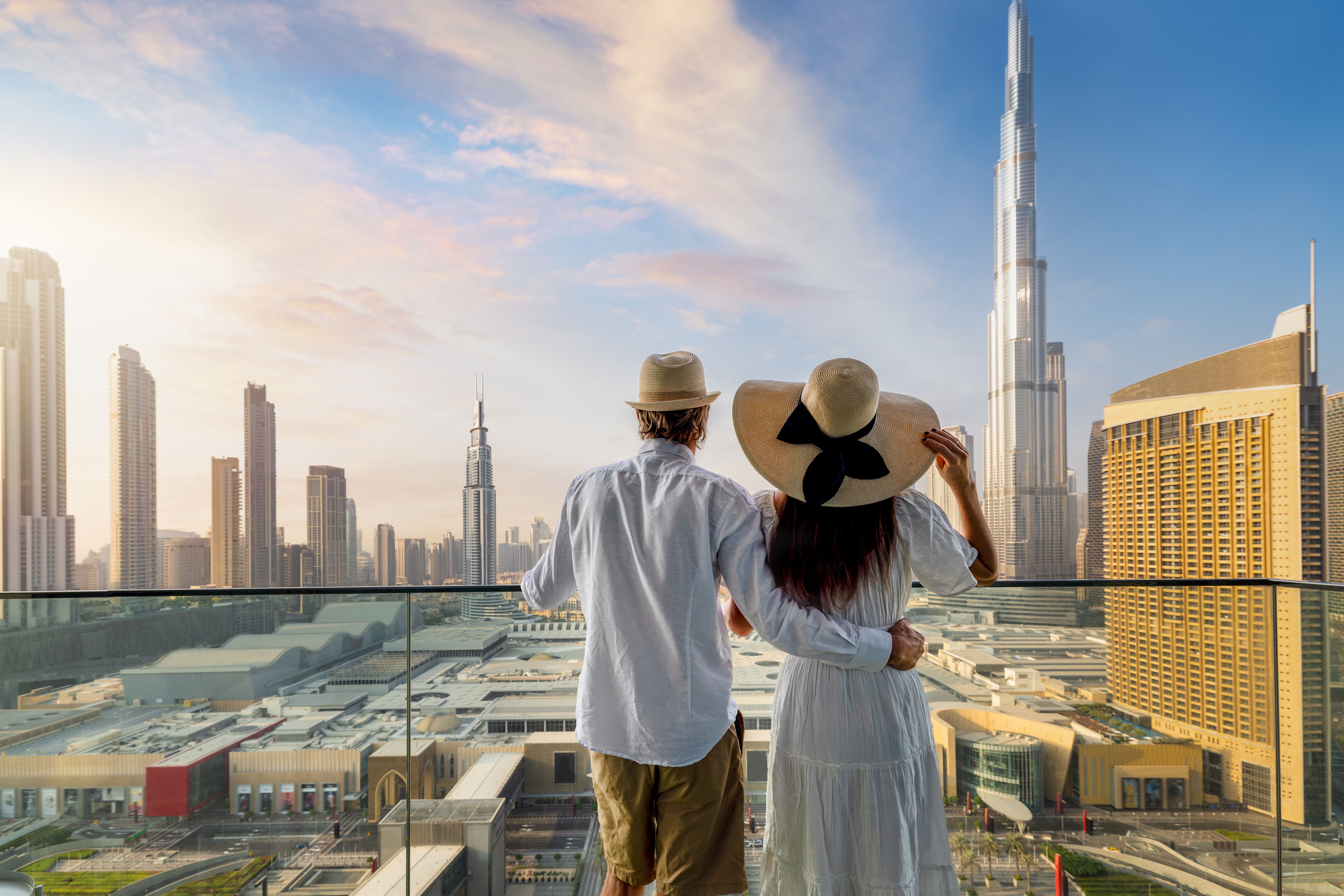 A tourist couple stands on a balcony and enjoys the sunrise over Dubai