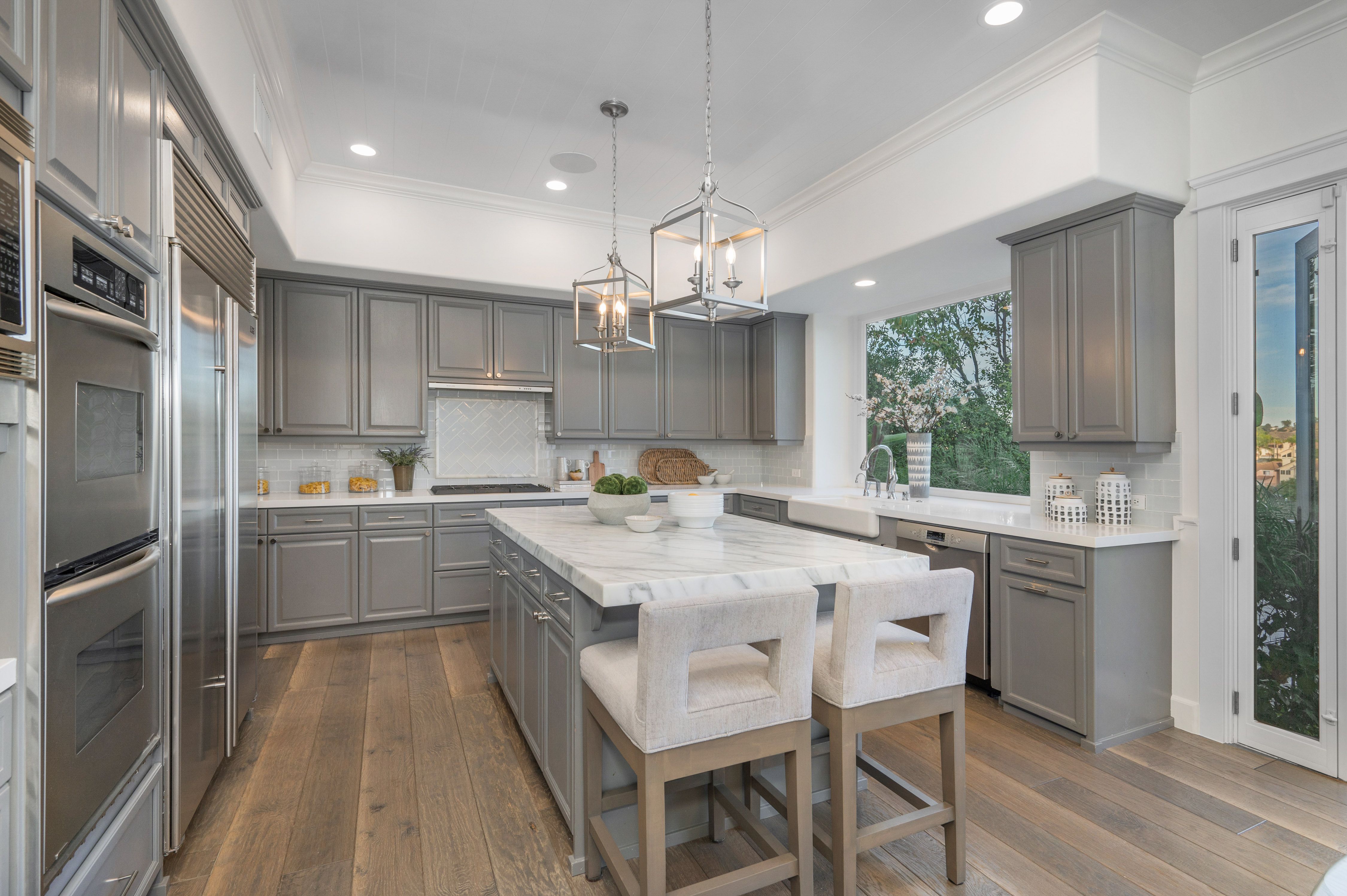 Modern kitchen with marble countertops, wooden floors, light gray cabinets, and an island