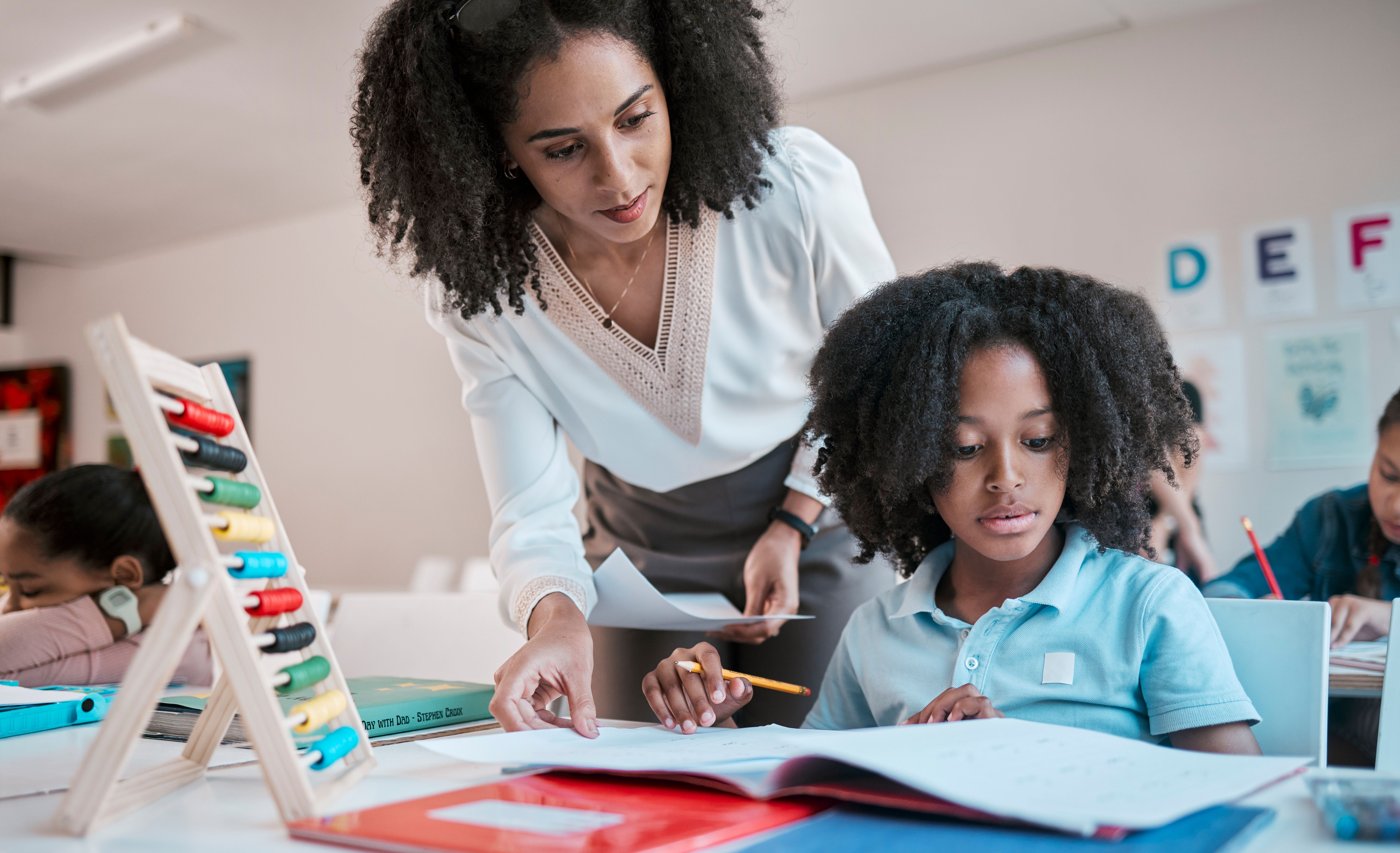 Math, education or teacher helping a child in a classroom with learning development, growth or studying. Writing, notebook or black woman teaching, talking or speaking to a young African boy student