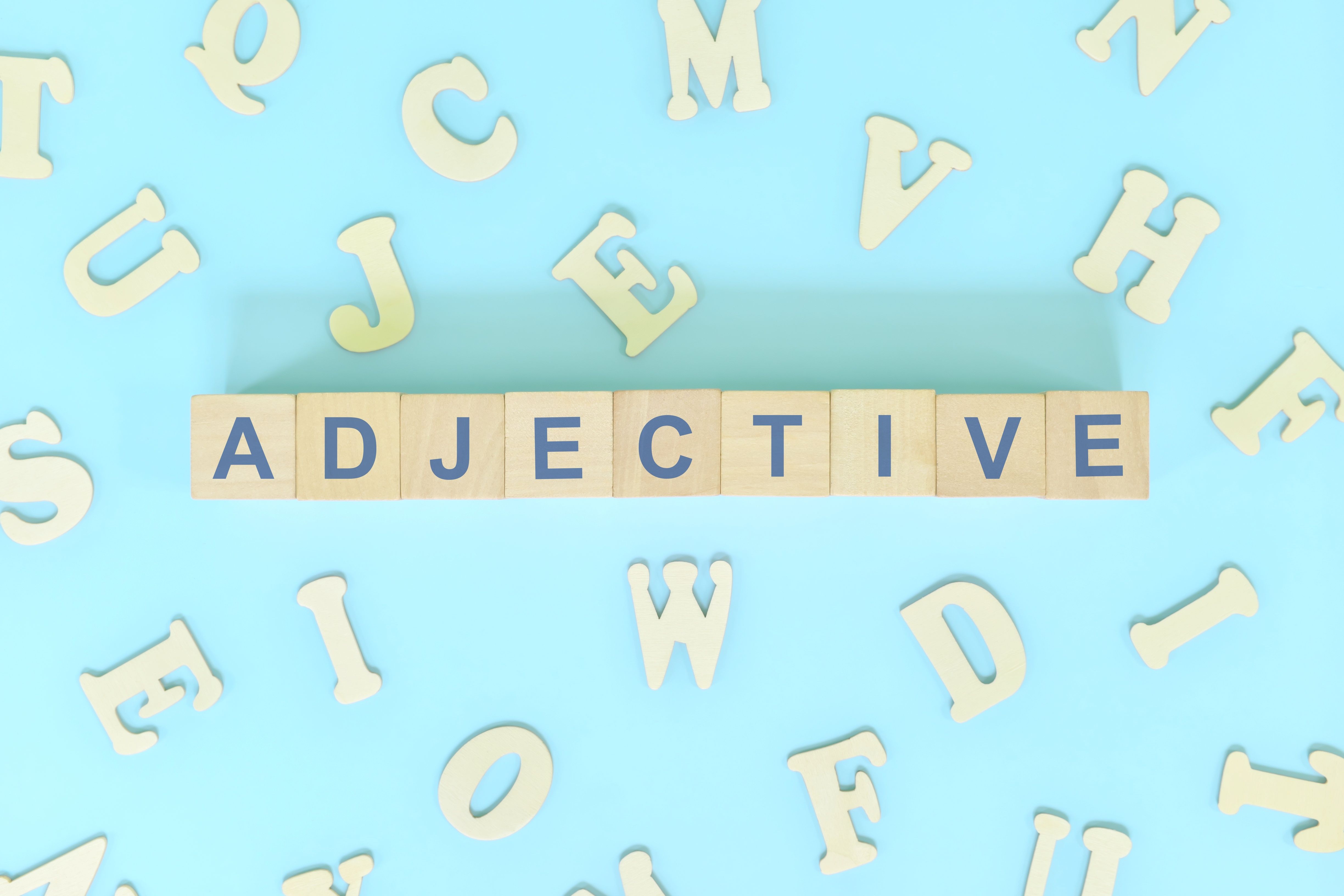 Adjective or adjectives concept in English grammar and learning class lesson. Wooden blocks typography word flat lay in blue background.