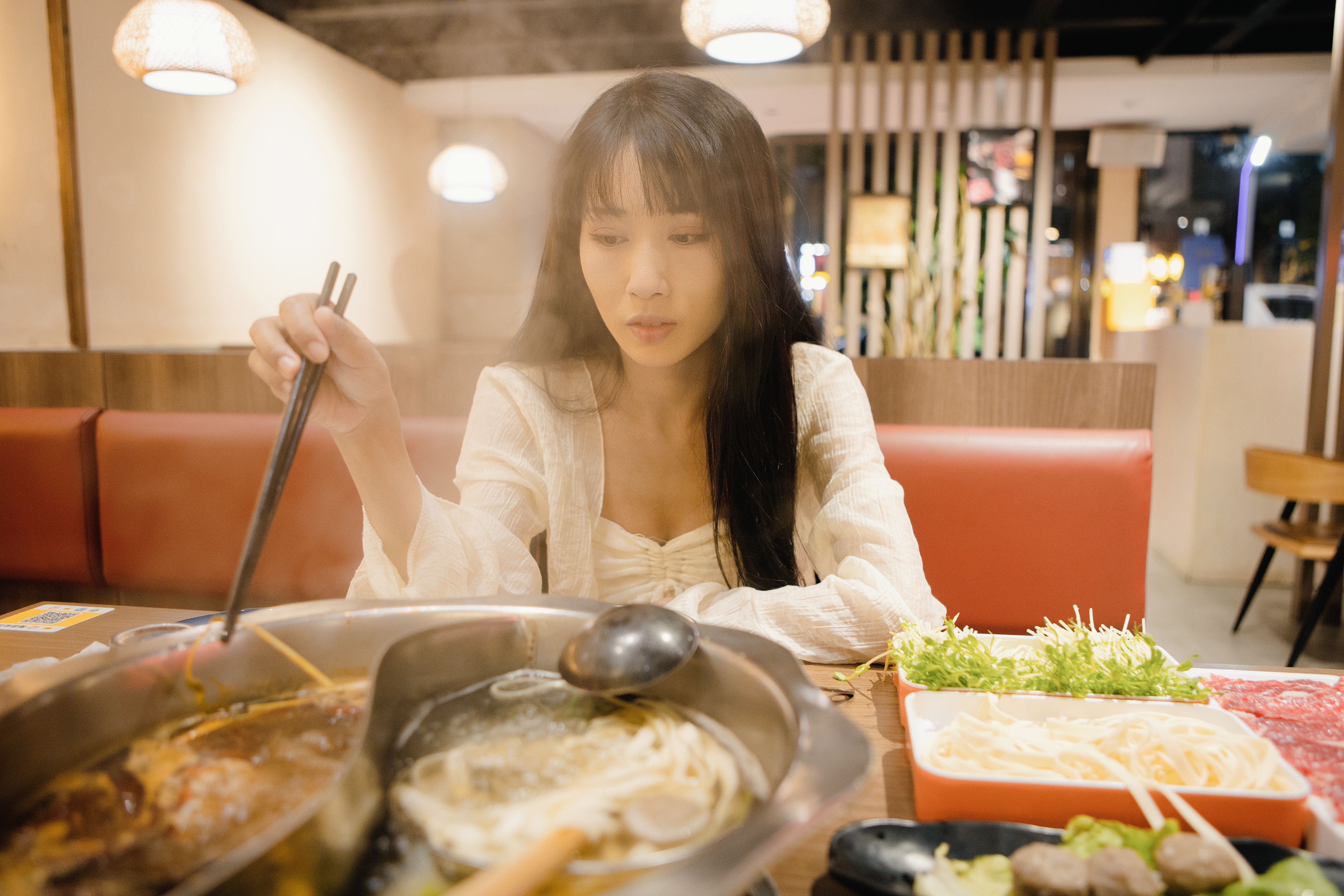 An Asian woman is eating beef hotpot, Chinese cuisine, and nightlife at a restaurant