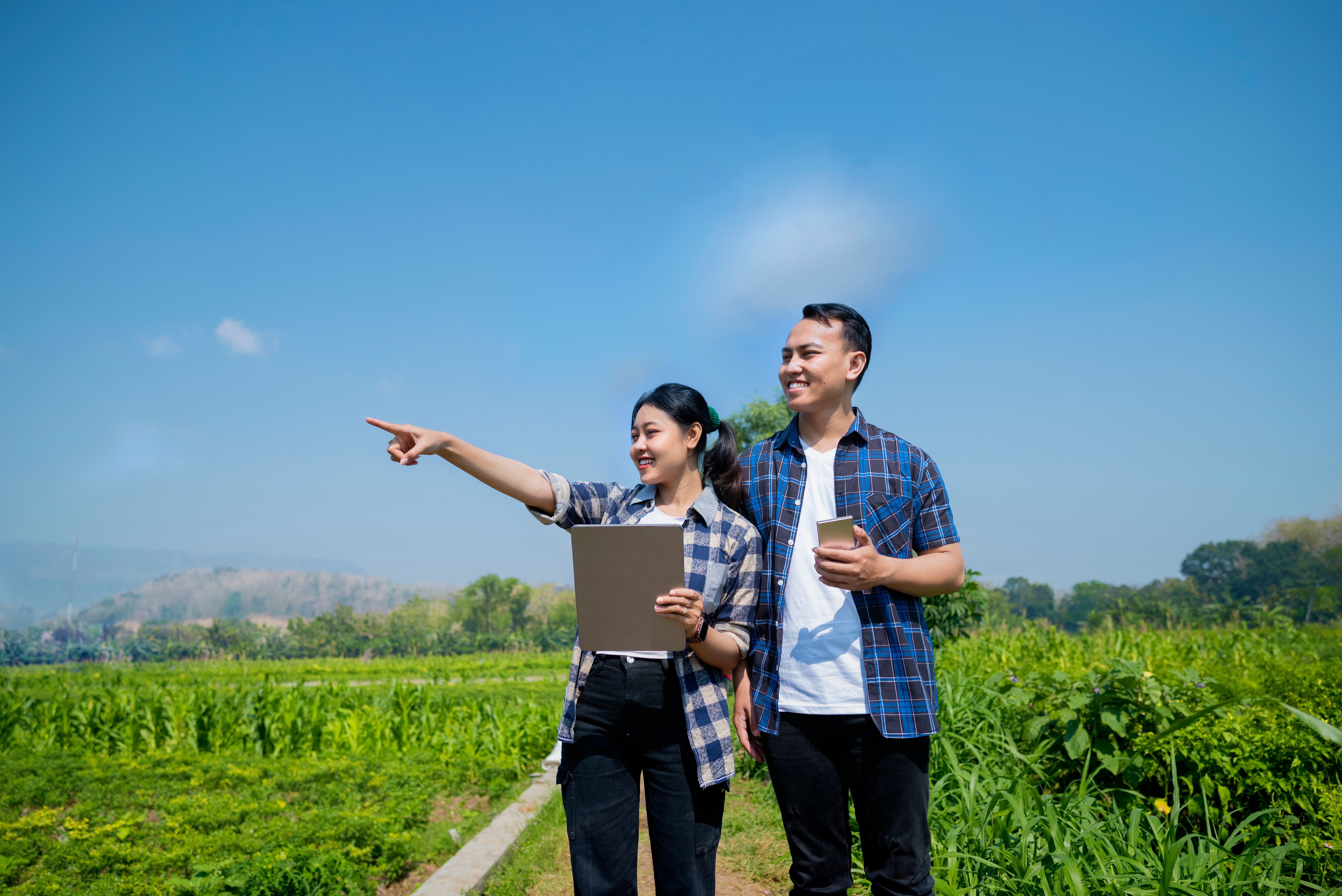 A man and a woman are looking at a tablet in a field