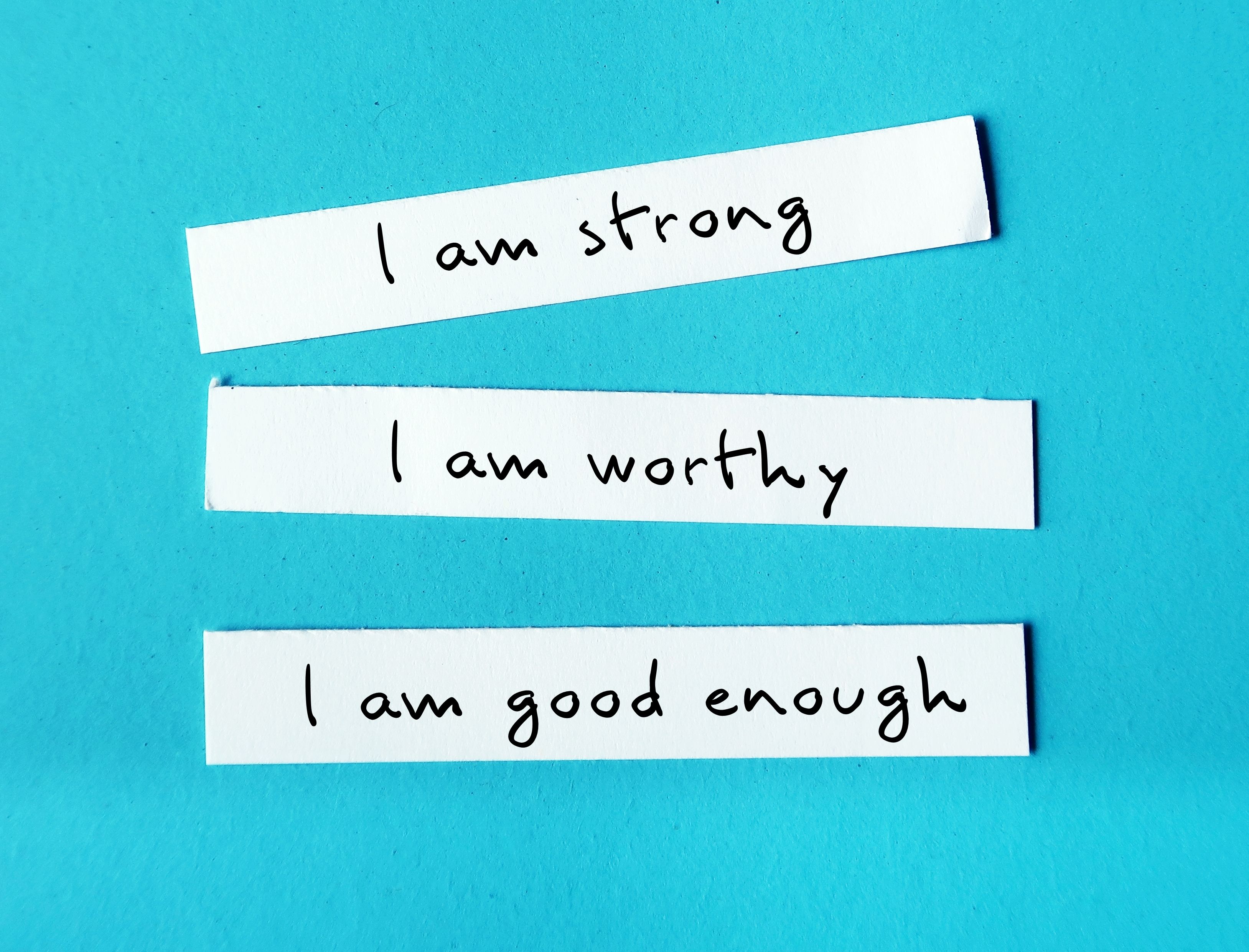 Three note paper on blue background with handwritten text I AM STRONG, I AM WORTHY, I AM ENOUGH - powerful self talk positive affirmations to boost self confidence self esteem
