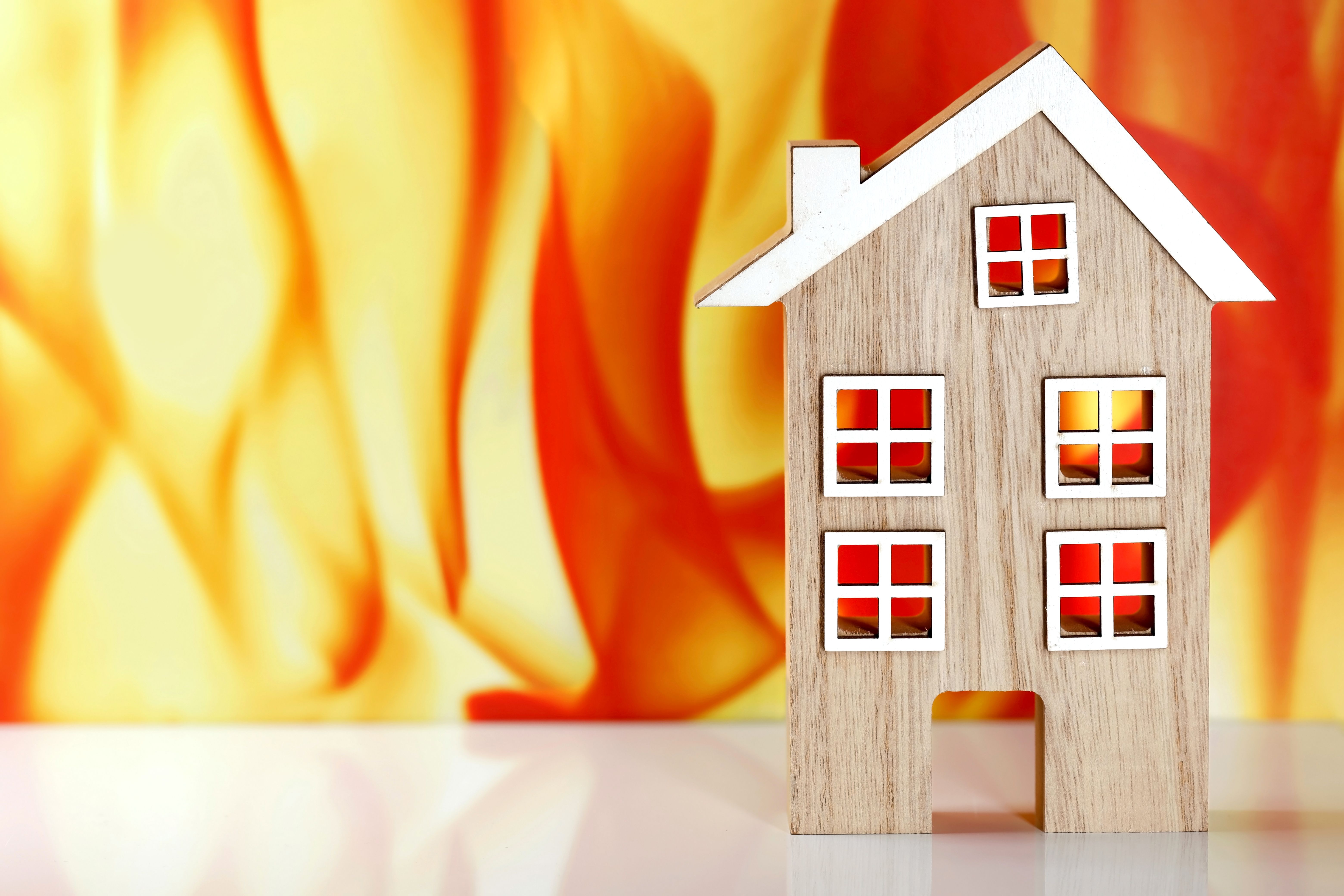 wooden model house in front of a fire flames background with copy space, concept image of fire safety or fire protection insurance