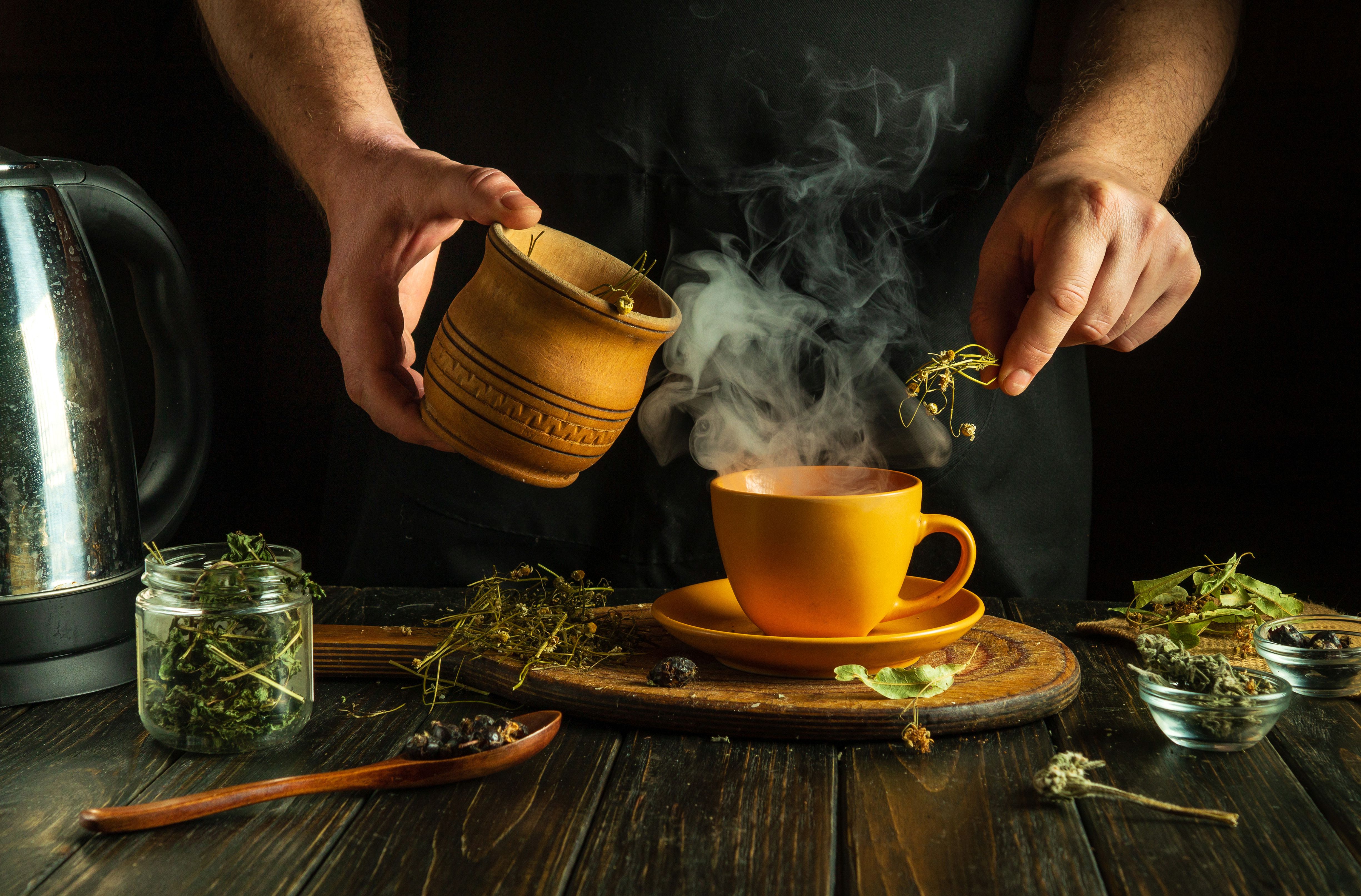 A man adds dry chamomile to a mug of boiling water to make medicinal tea for a cold. Traditional medicine concept or making healthy aromatic tea