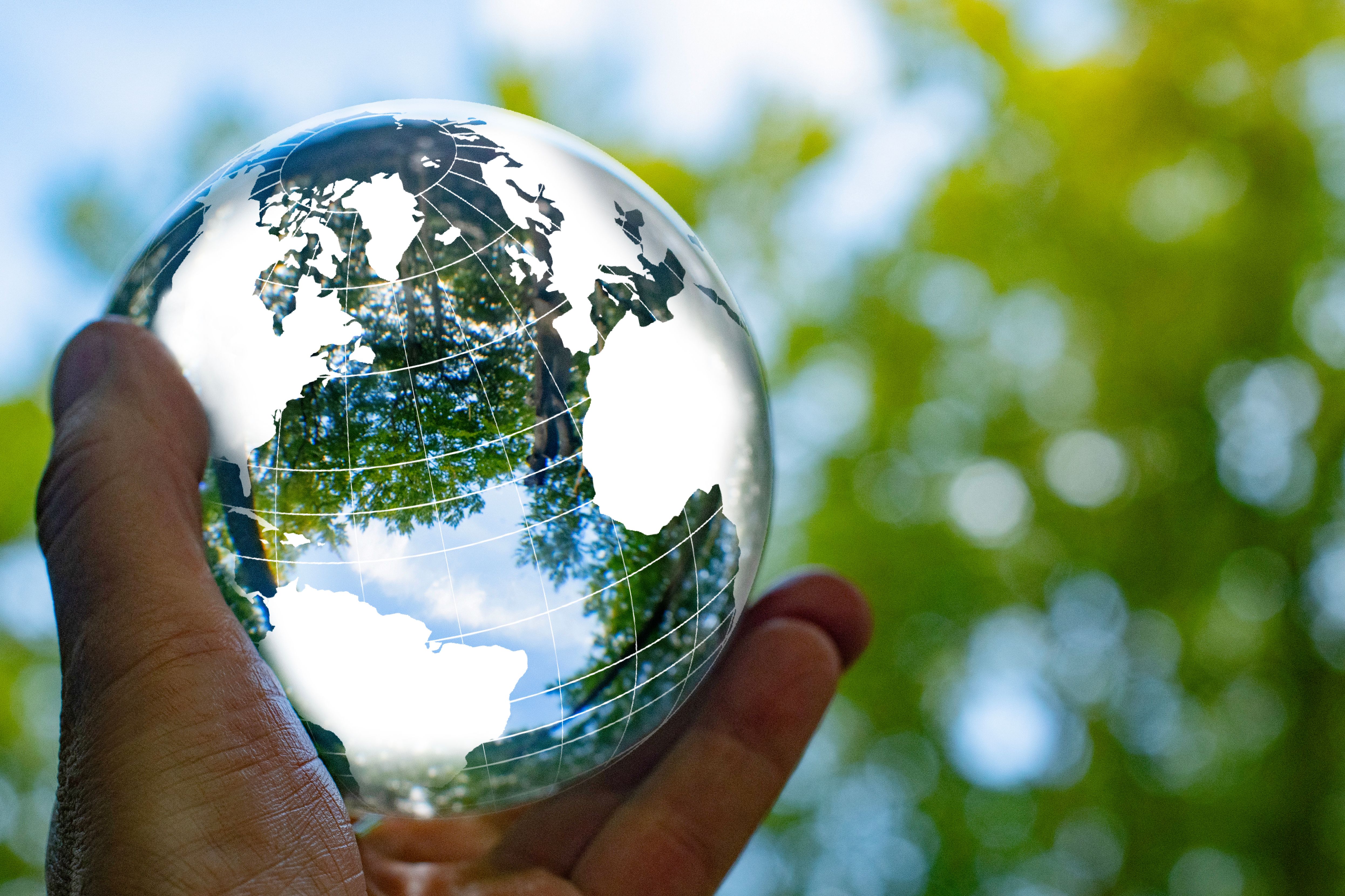 Focus on taking care of nature and the climate shown with a globe around  a crystal ball with nature reflected  inside and outside the ball. The ball is held by one hand.