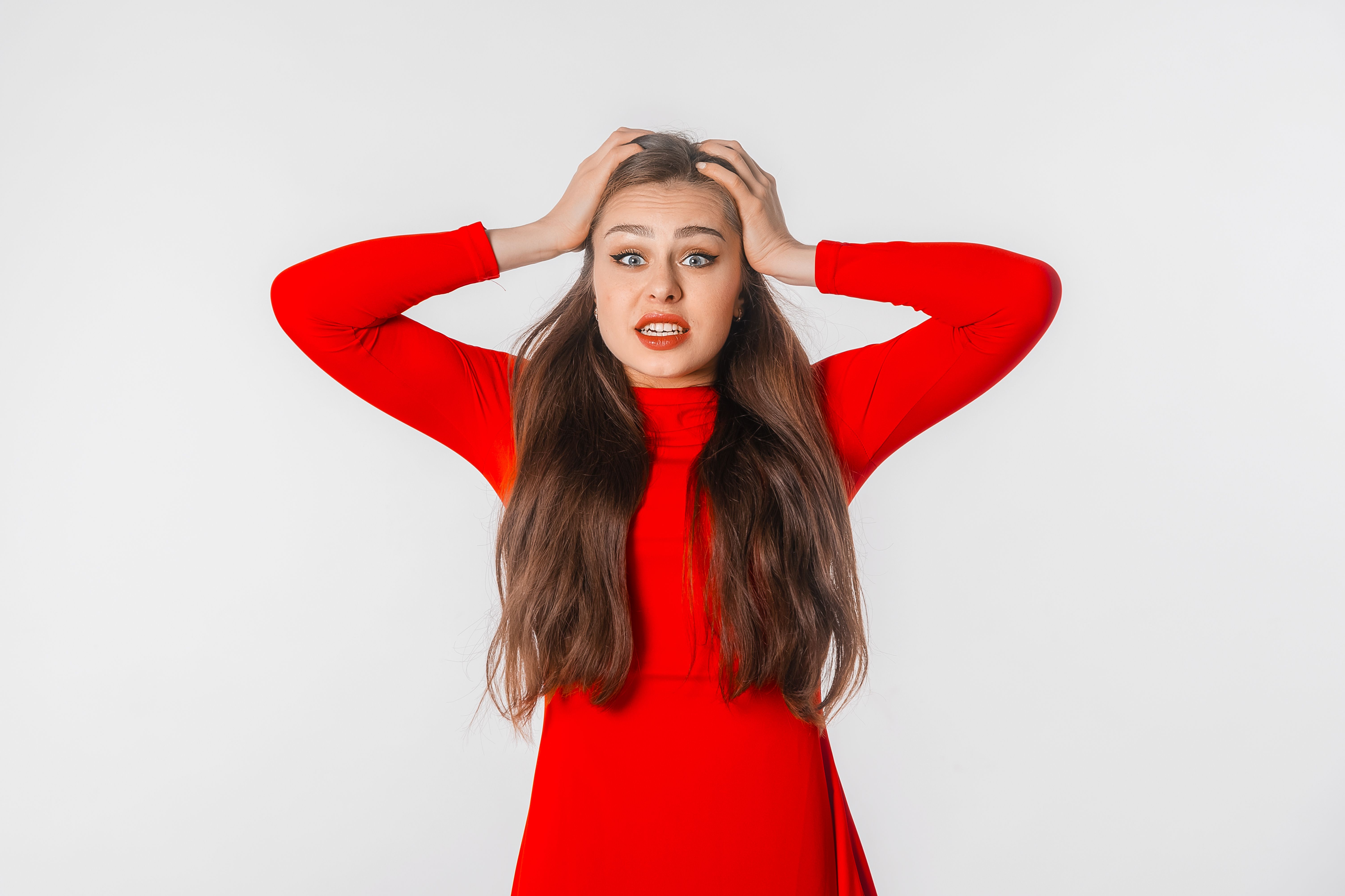 Portrait of the shocked anxious young woman in panic, holding hands on head and worrying, standing frustrated and scared against white studio background. Psychology, depression, bad mood, stress