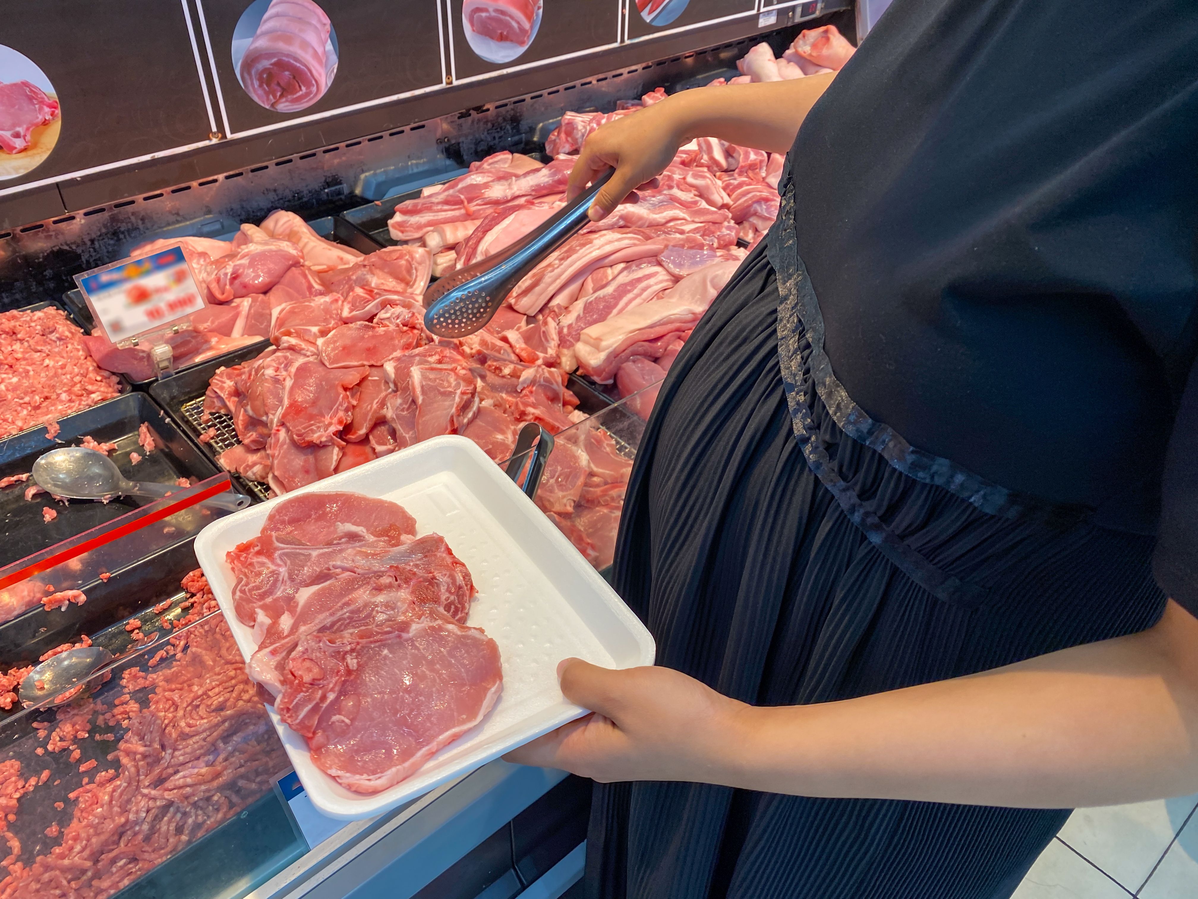 Pregnant woman with big belly buying pork meat in supermarket