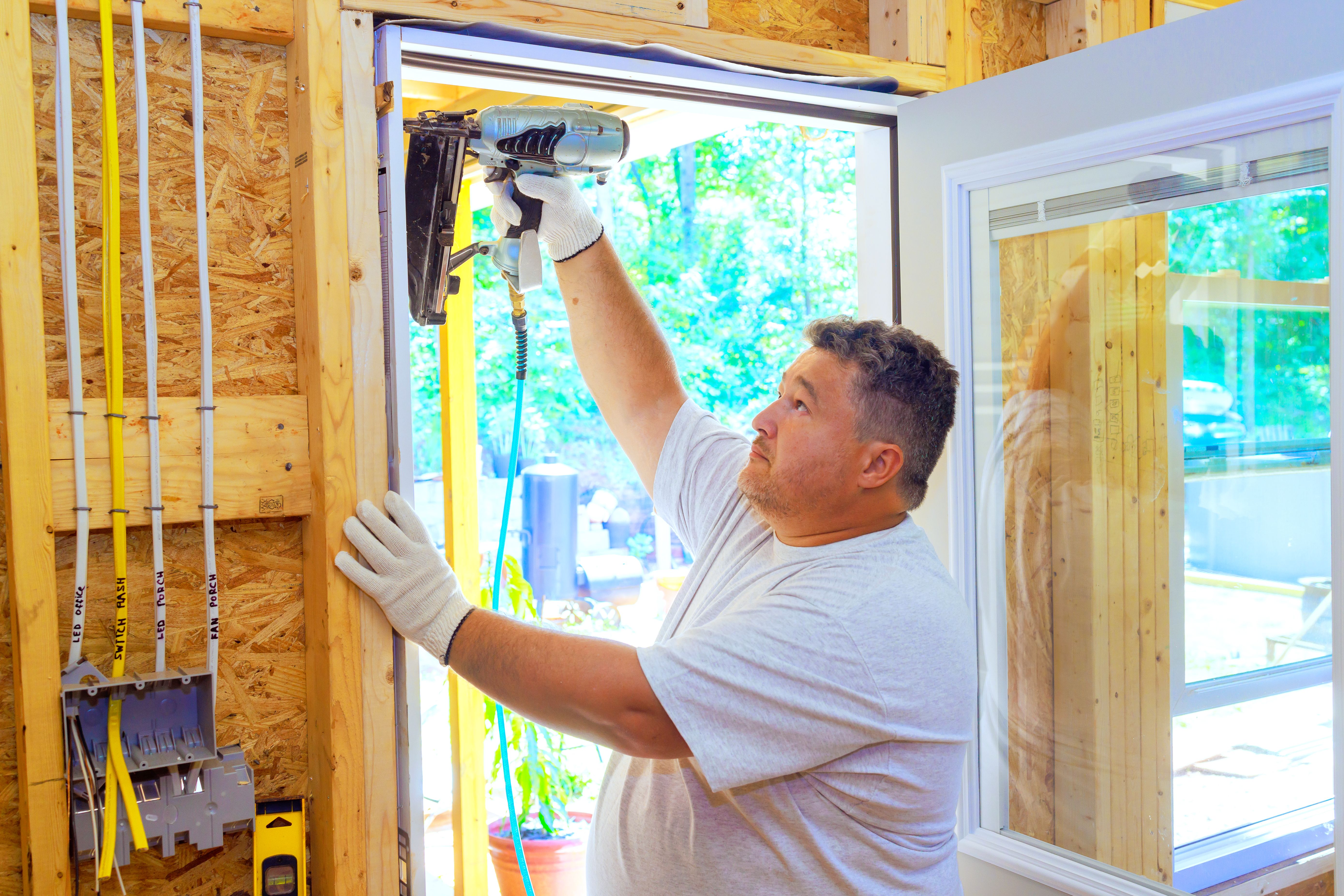 Carpenter is using pneumatic nail gun to install new front door for a new house
