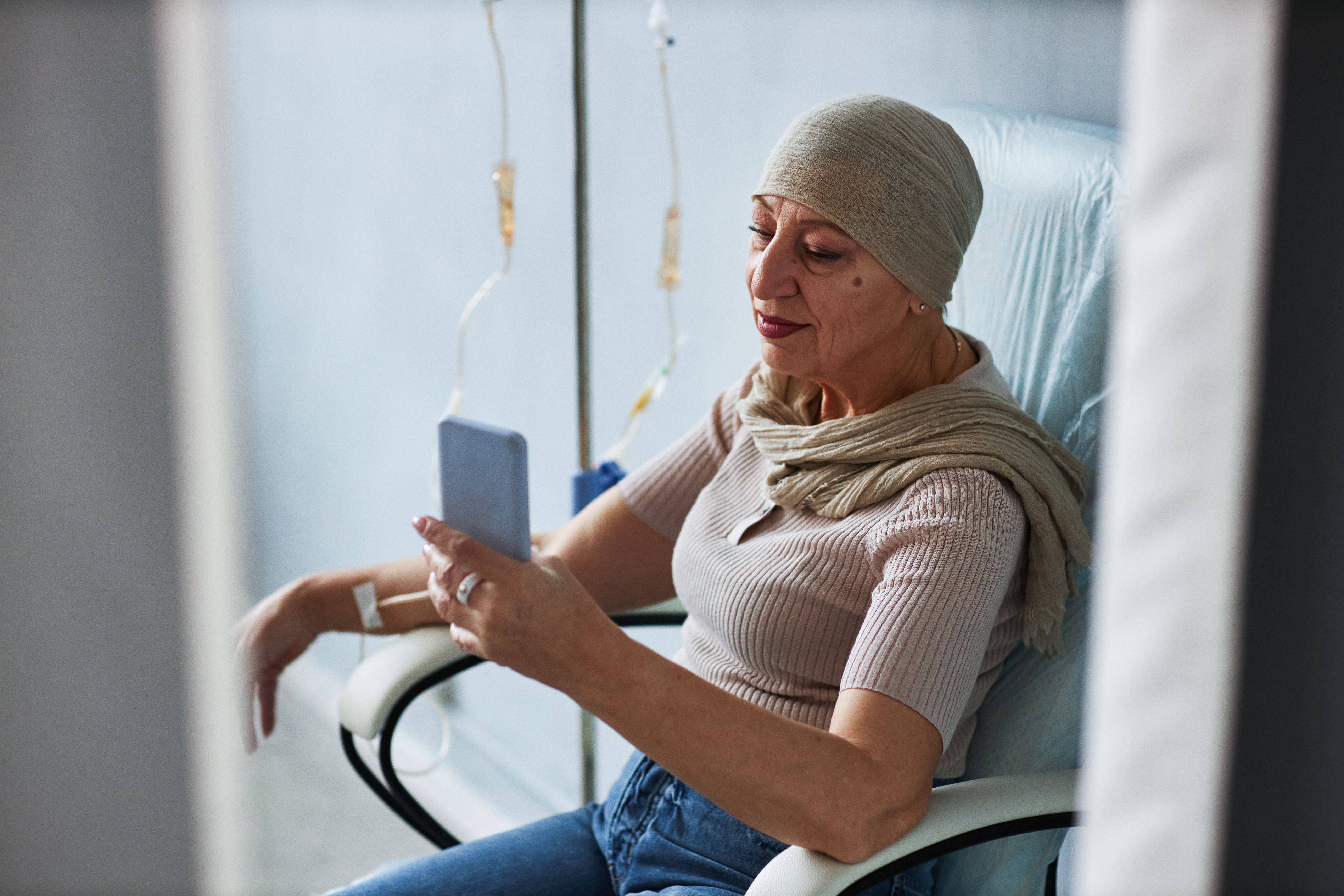 Side view senior woman with IV drip and using smartphone