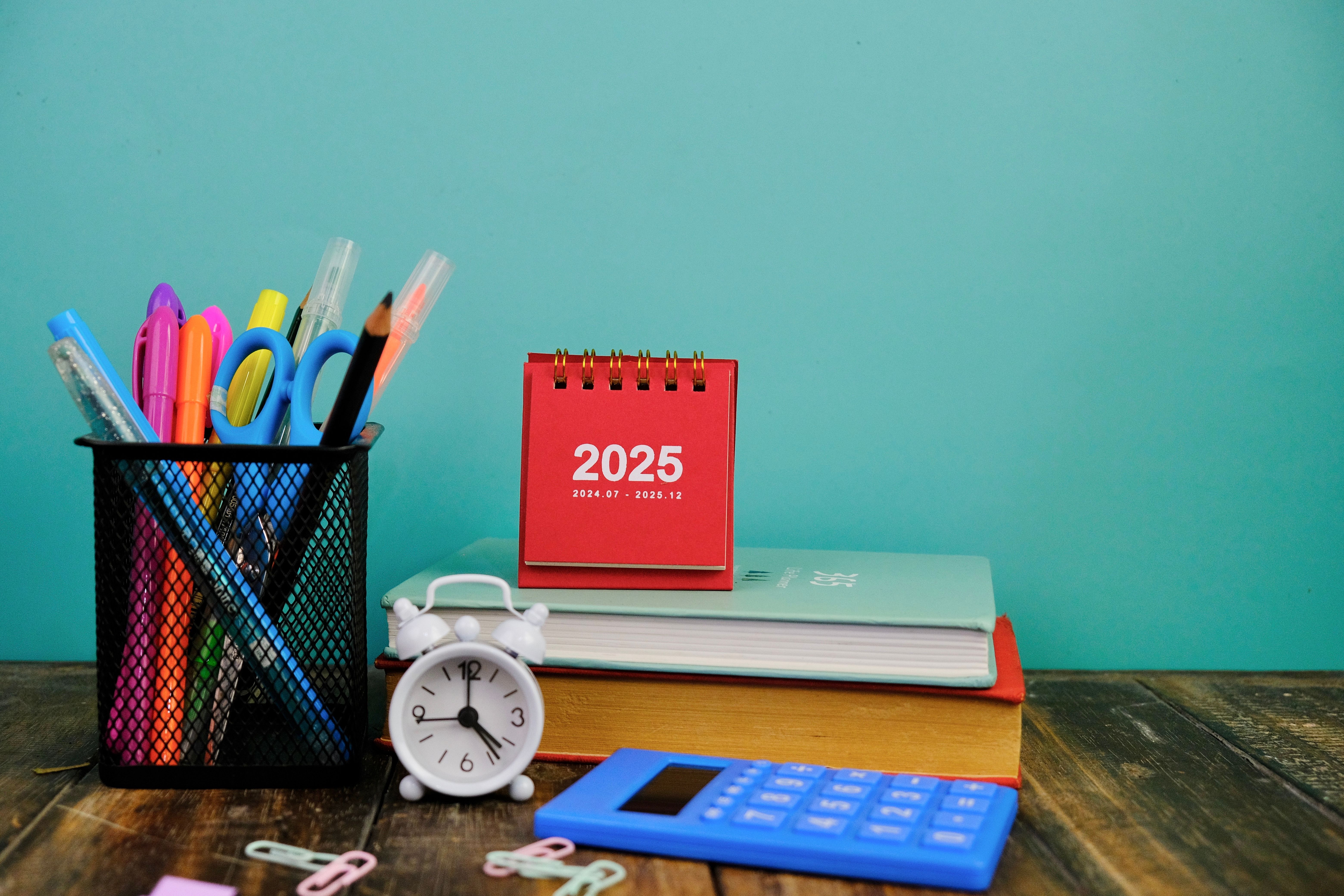 Calendar and new year concept. colorful pens in the metal pen holder sitting next to small alarm clock, books and mini calendar of 2025 Calendar and new year concept. colorful pens in the metal pen holder sitting next to small alarm clock, books and mini calendar of 2025