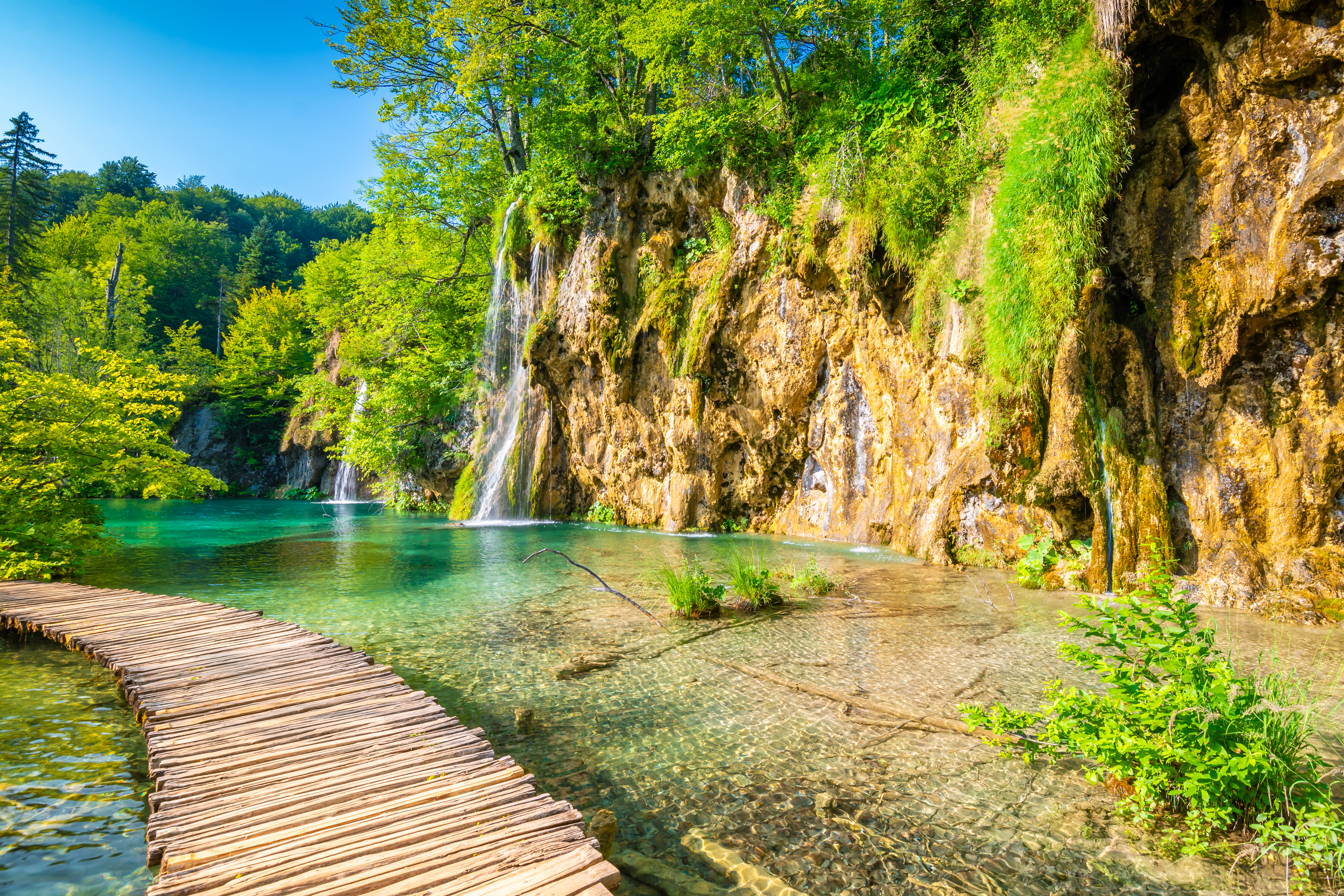 Wooden footpath at Plitvice national park, Croatia. Pathway in the forest near the lake and waterfall. Fresh beautiful nature, peaceful place. Famous tourist destination. Wooden footpath at Plitvice national park, Croatia. Pathway in the forest near the lake and waterfall. Fresh beautiful nature, peaceful place. Famous tourist destination.