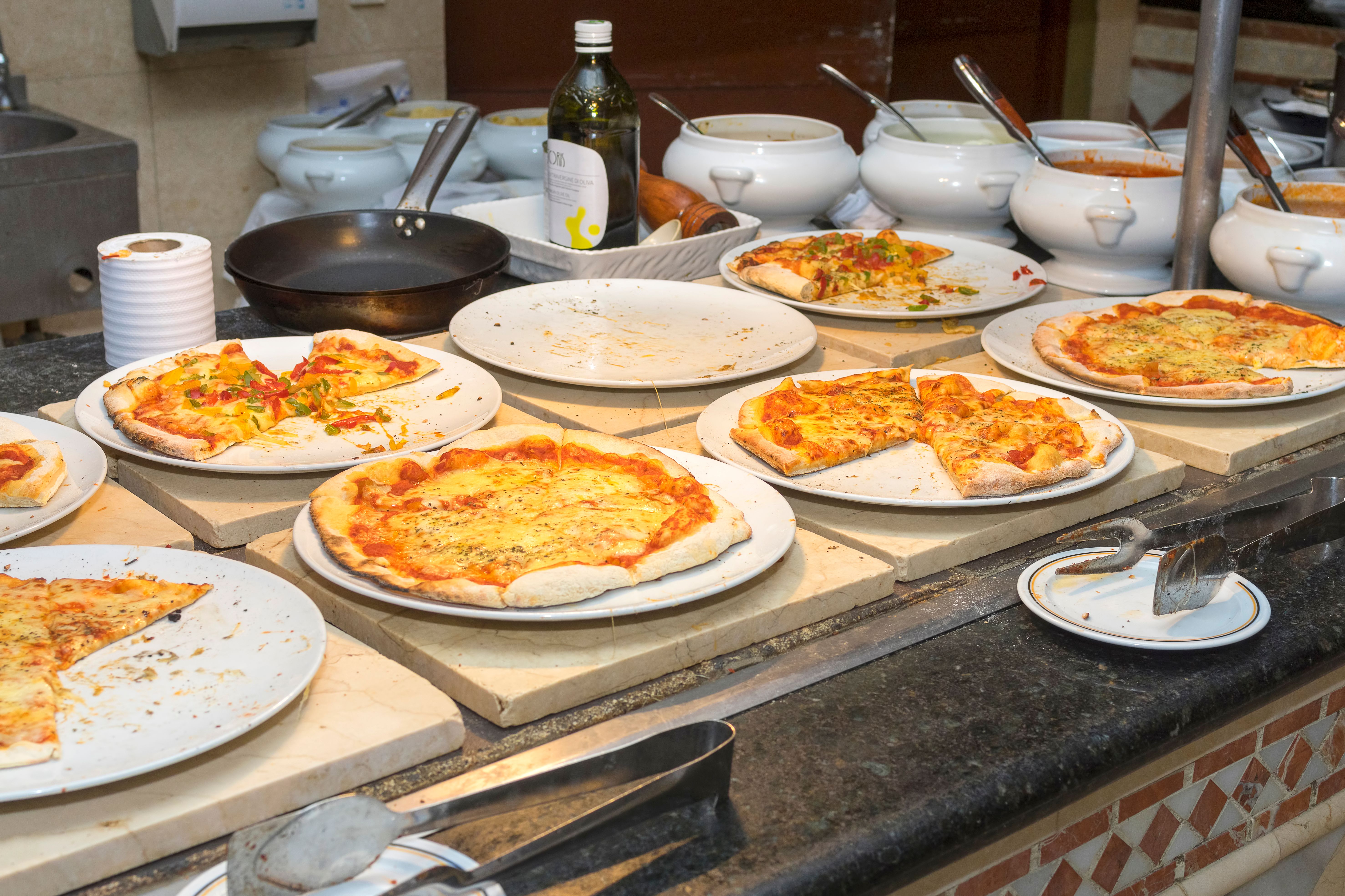 Different kinds of pizza on white plates on a buffet