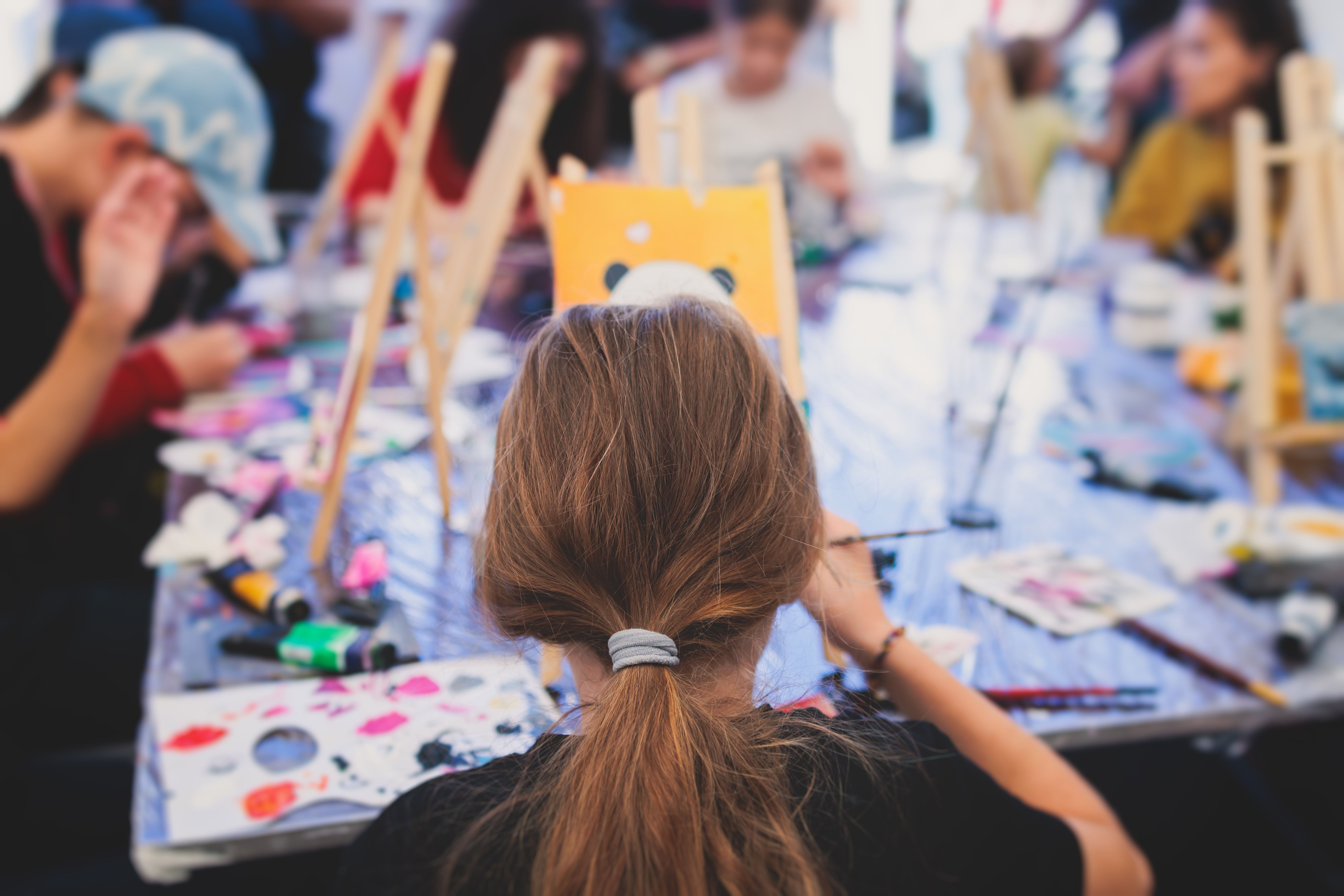 Process of painting, group class of young talented kids students with painting easels, and canvases during lesson of watercolour painting outdoors, drawing class for children in art school