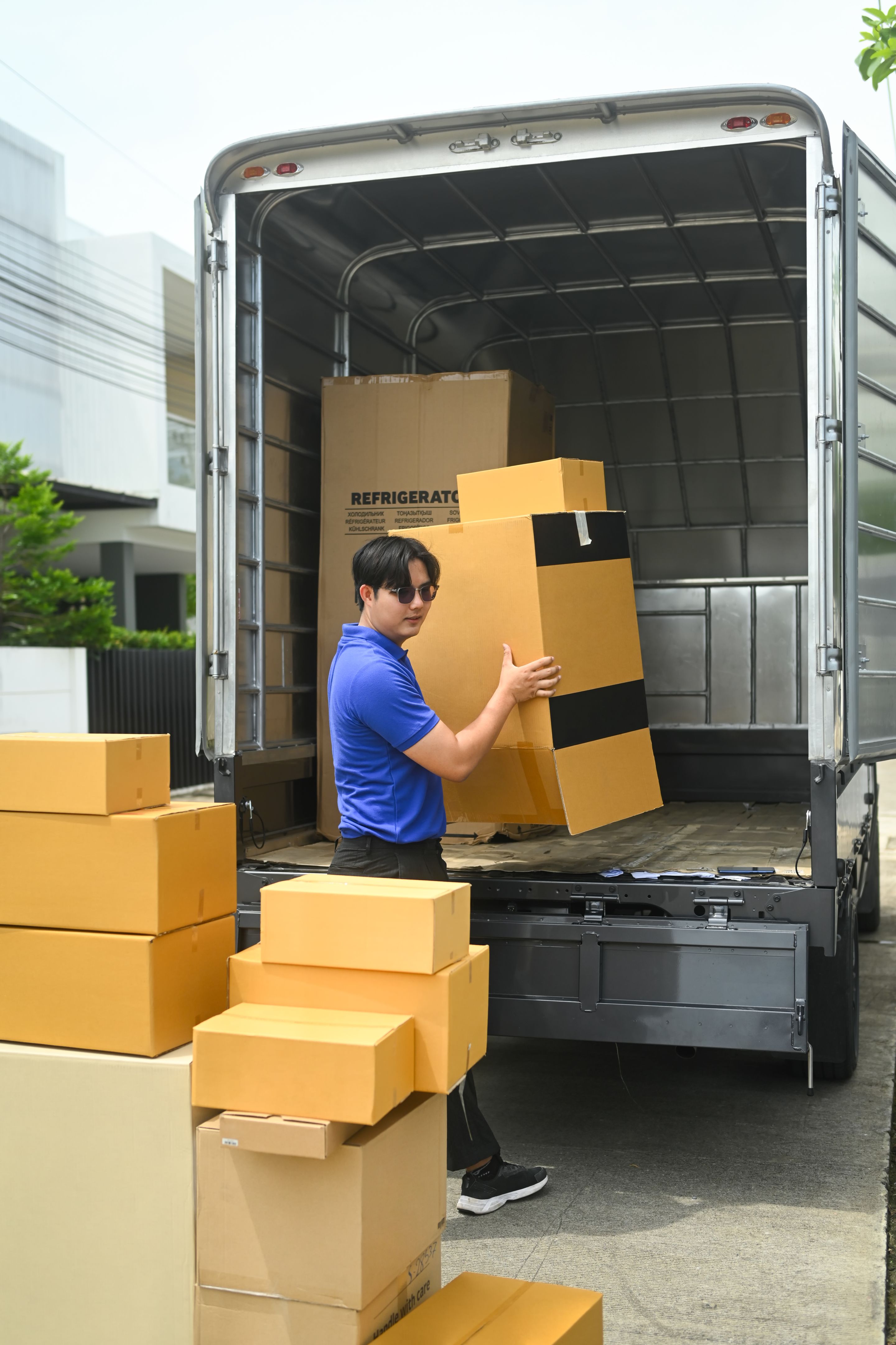 Delivery man in uniform unloading cardboard boxes from from van. Moving service and transportation concept
