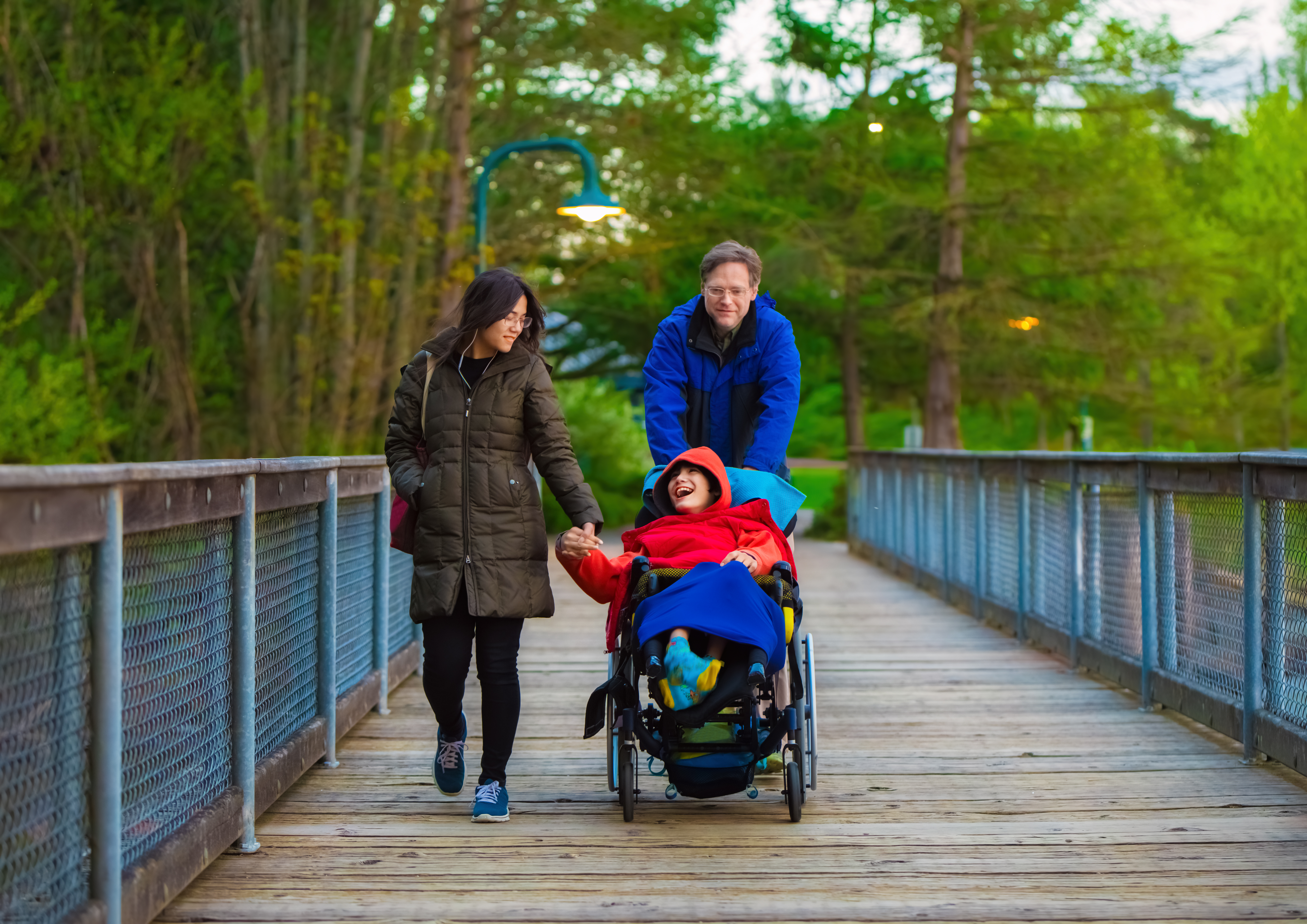 Disabled child in wheelchair at park with father and sister
