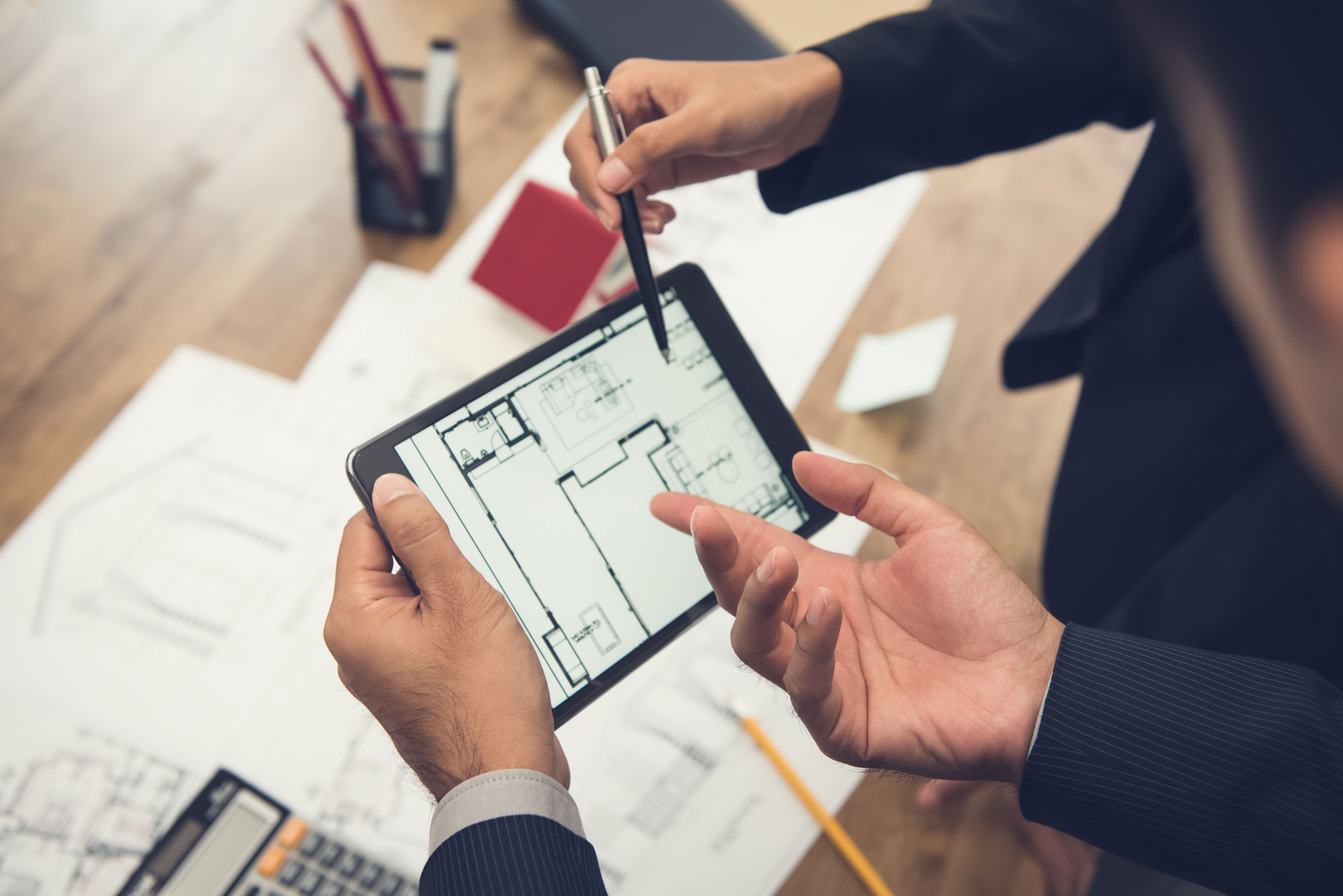 Real estate agent with client or architect team checking a housing model and its blueprints digitally using a tablet Real estate agent with client or architect team checking a housing model and its blueprints digitally using a tablet