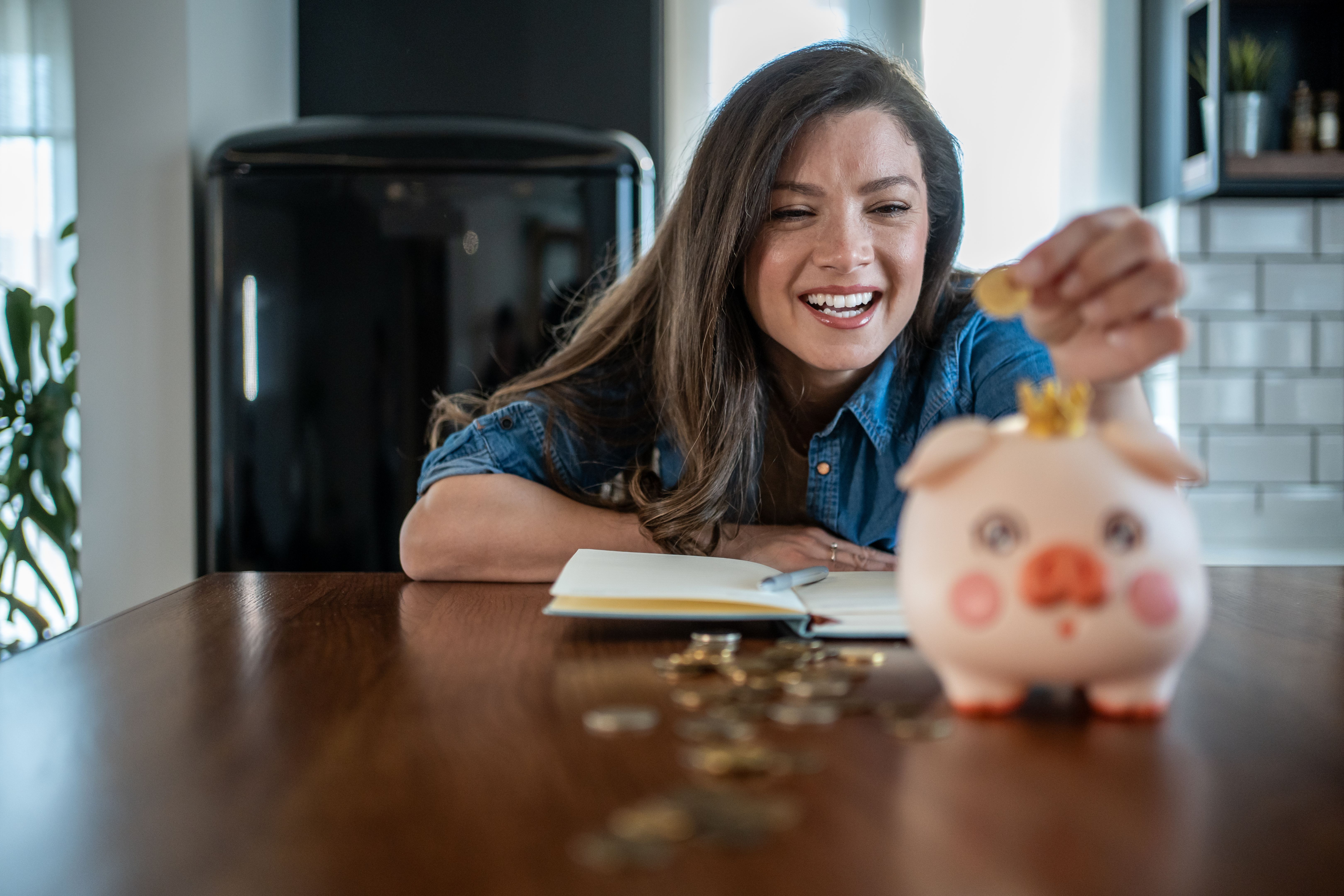 Smiling woman saving money in piggy bank at home
