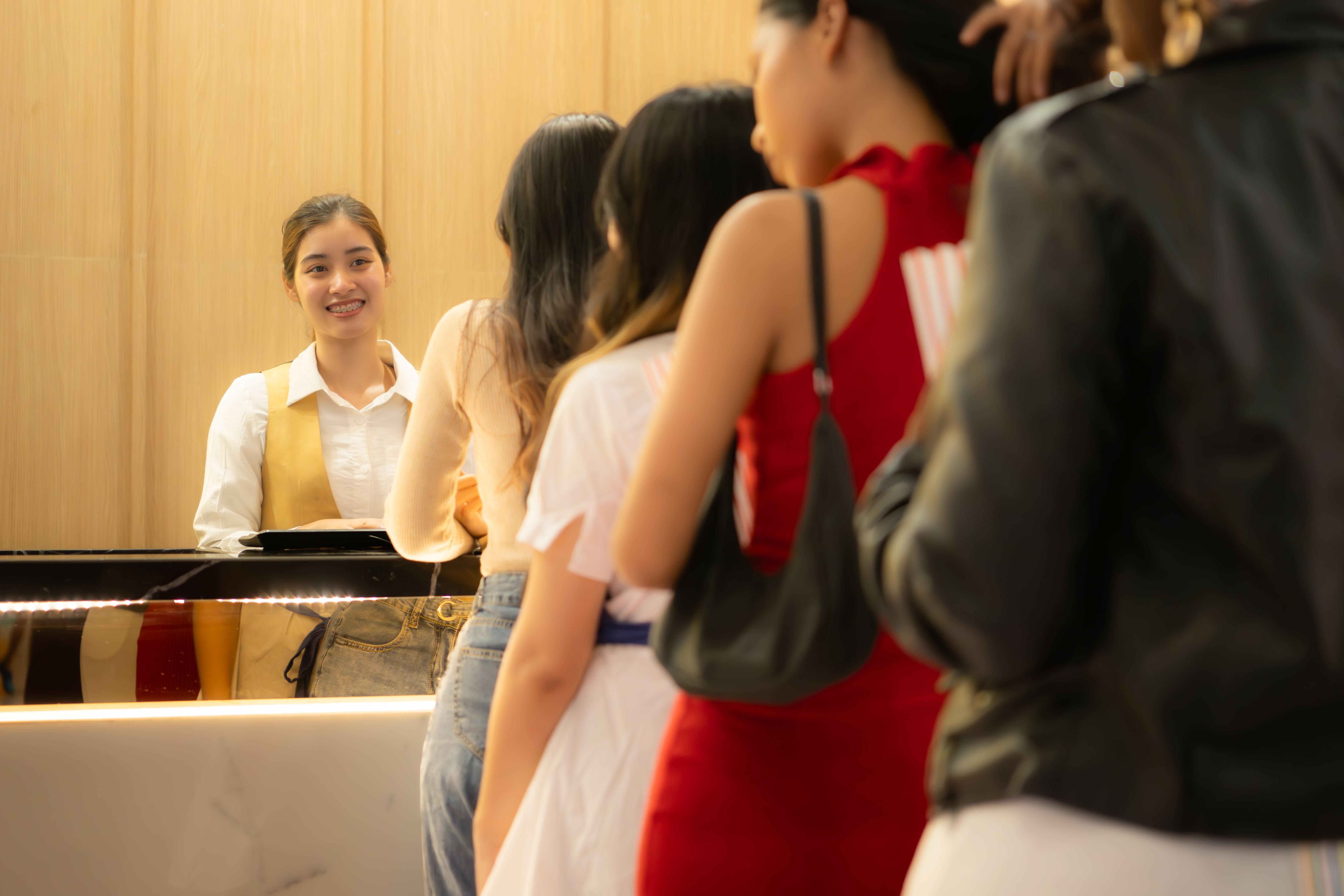 Young asian woman standing in line to buy movie tickets and in hand popcorn and drink, Smiling ticket salesman serving.