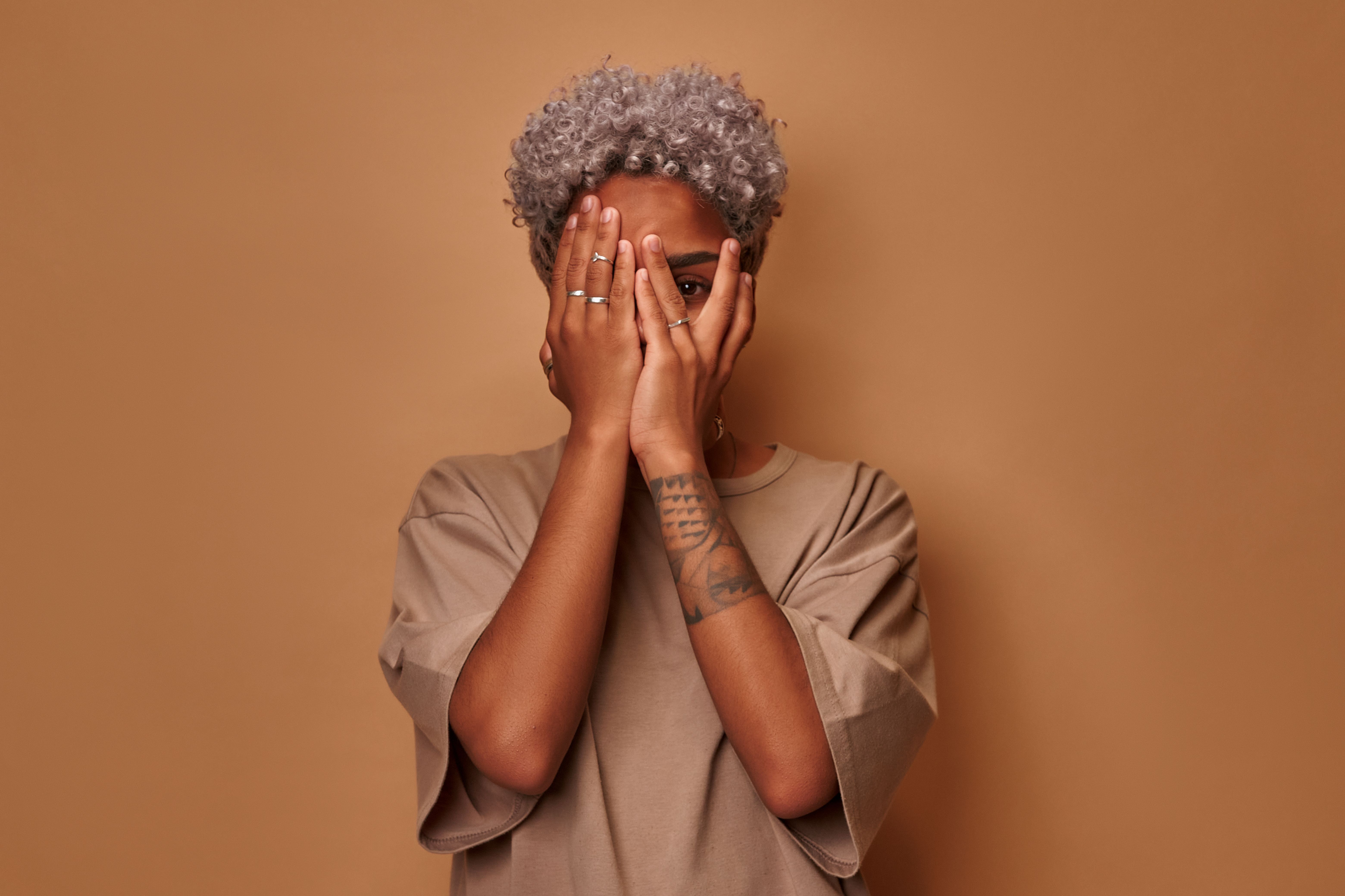 Frightened dark skinned woman covers face with palms peeks through fingers Frightened dark skinned woman covers face with palms peeks through fingers