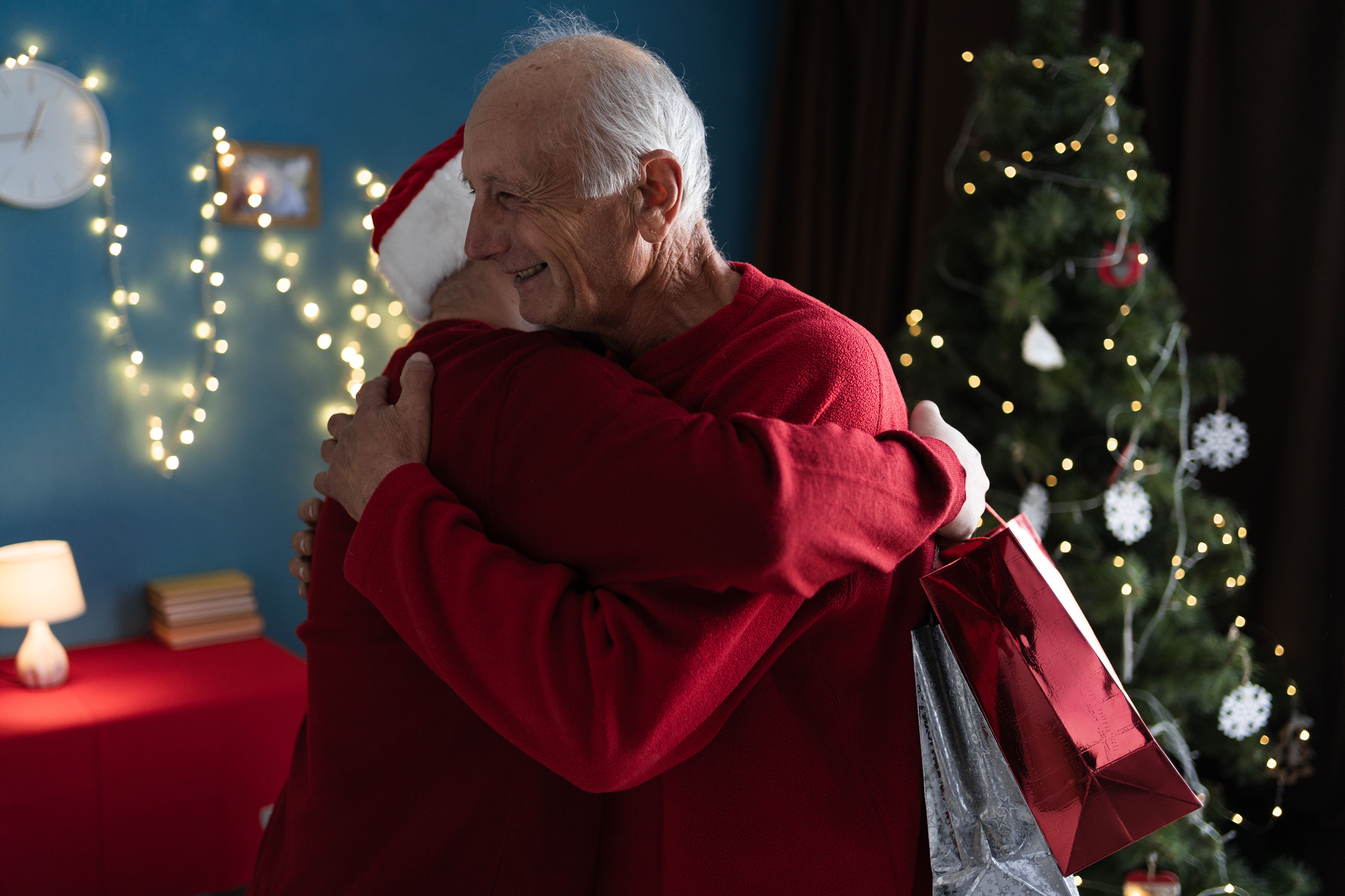 An elderly father hugs his son who came to visit him on Christmas or New Year with gifts. The concept of family and holidays