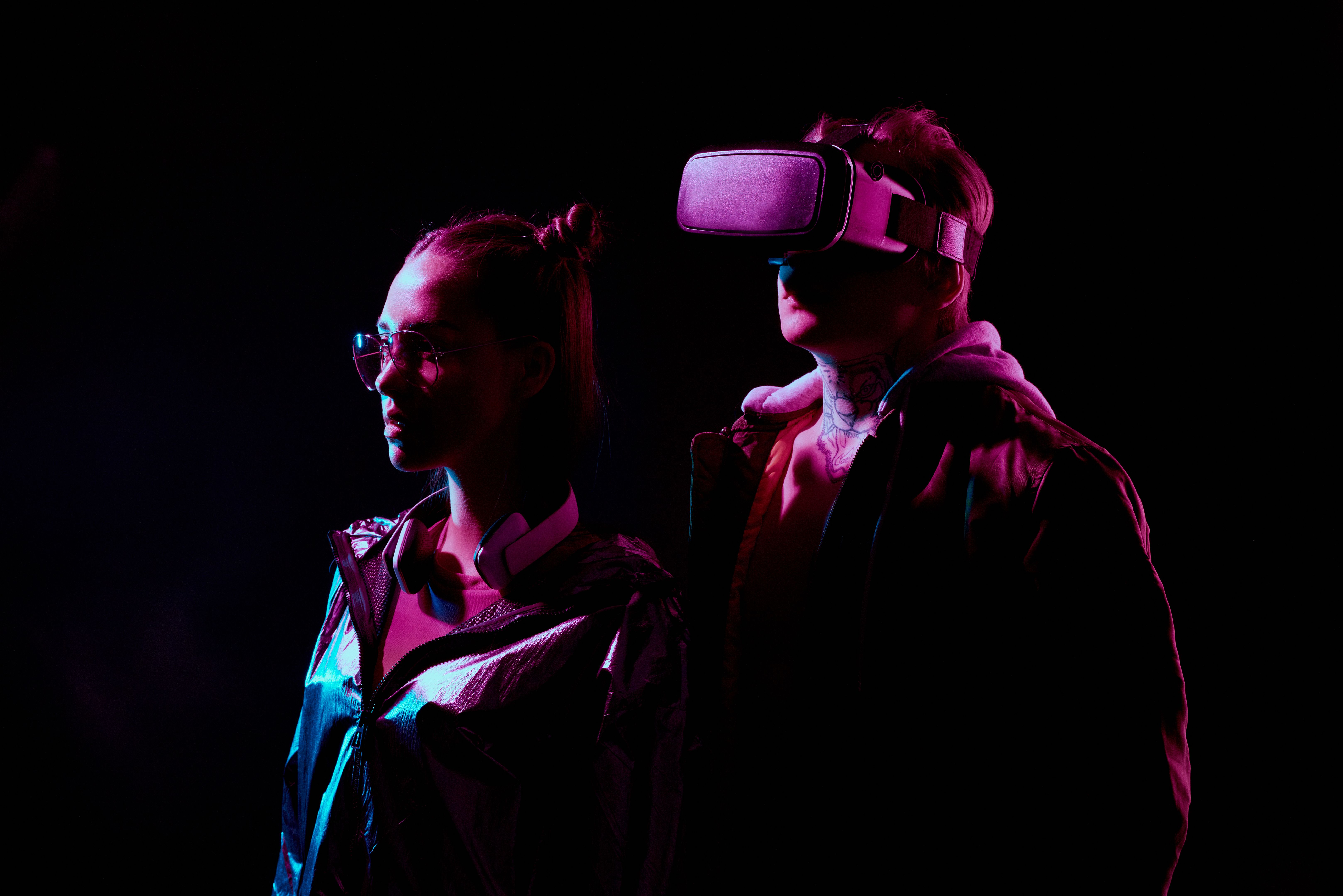 Side view of serious young couple using virtual reality simulator in darkness