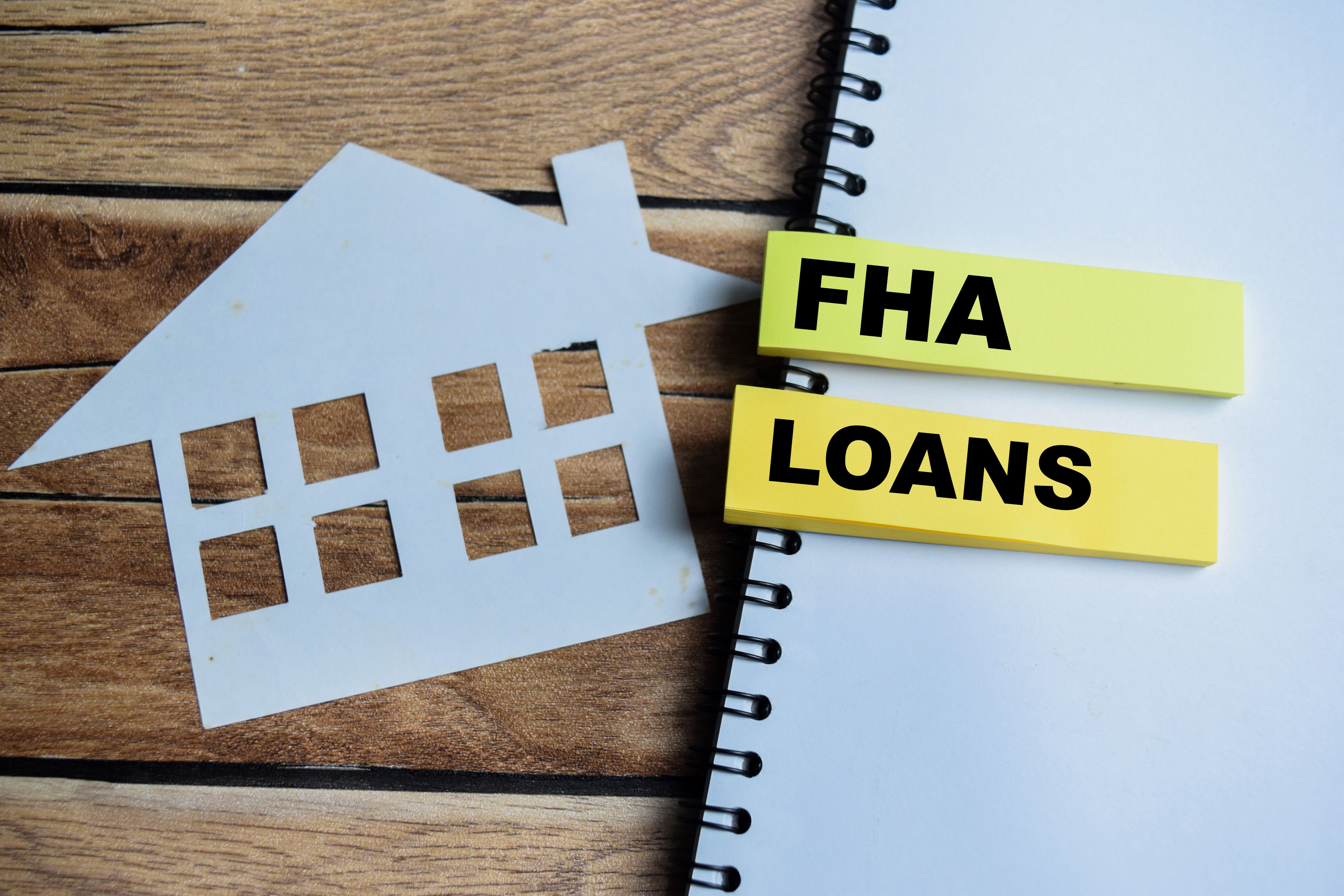 Concept of FHA Loans write on sticky notes isolated on Wooden Table.