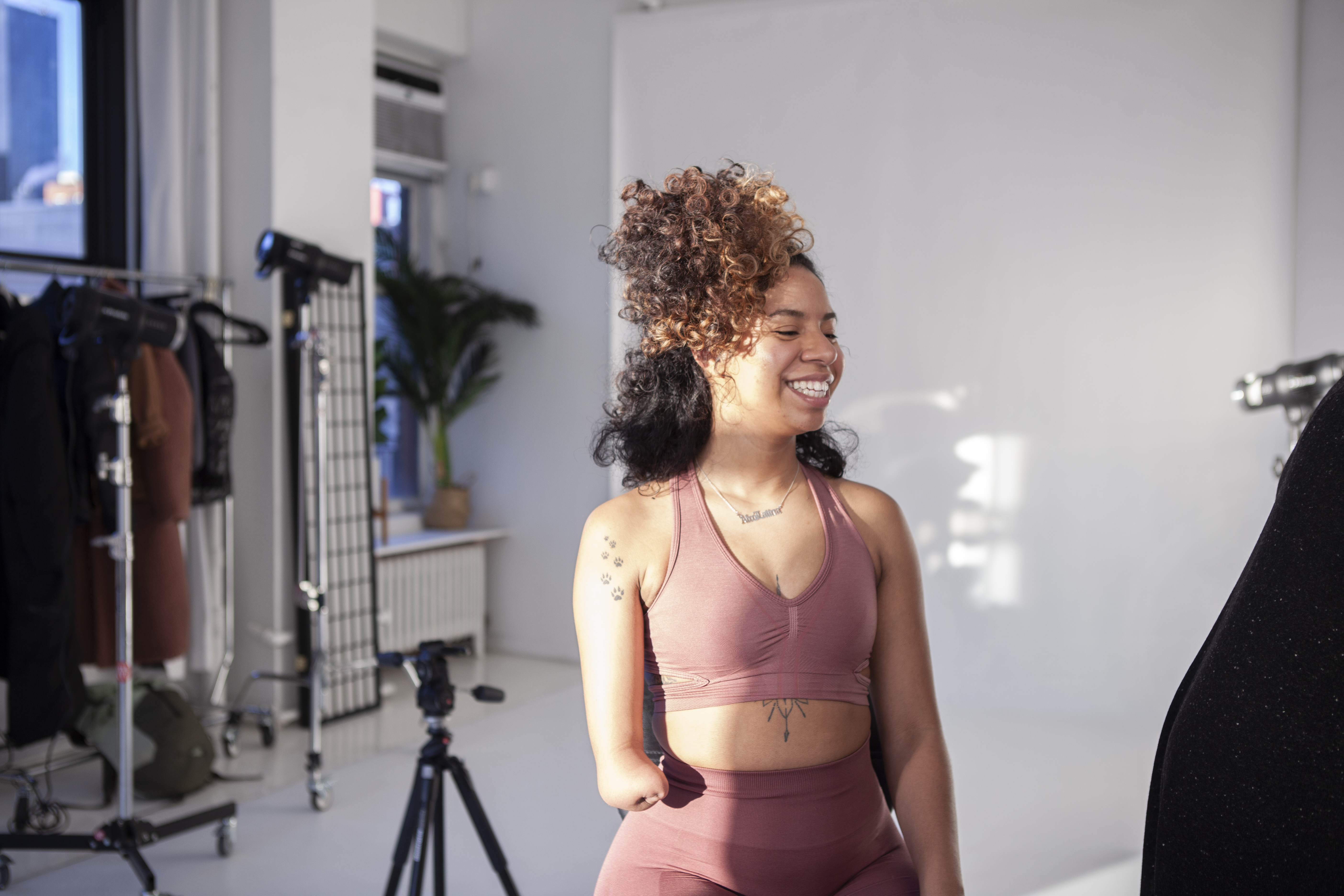 Candid behind the scenes portrait of a woman with a limb difference smiling in a studio during a professional modeling session.