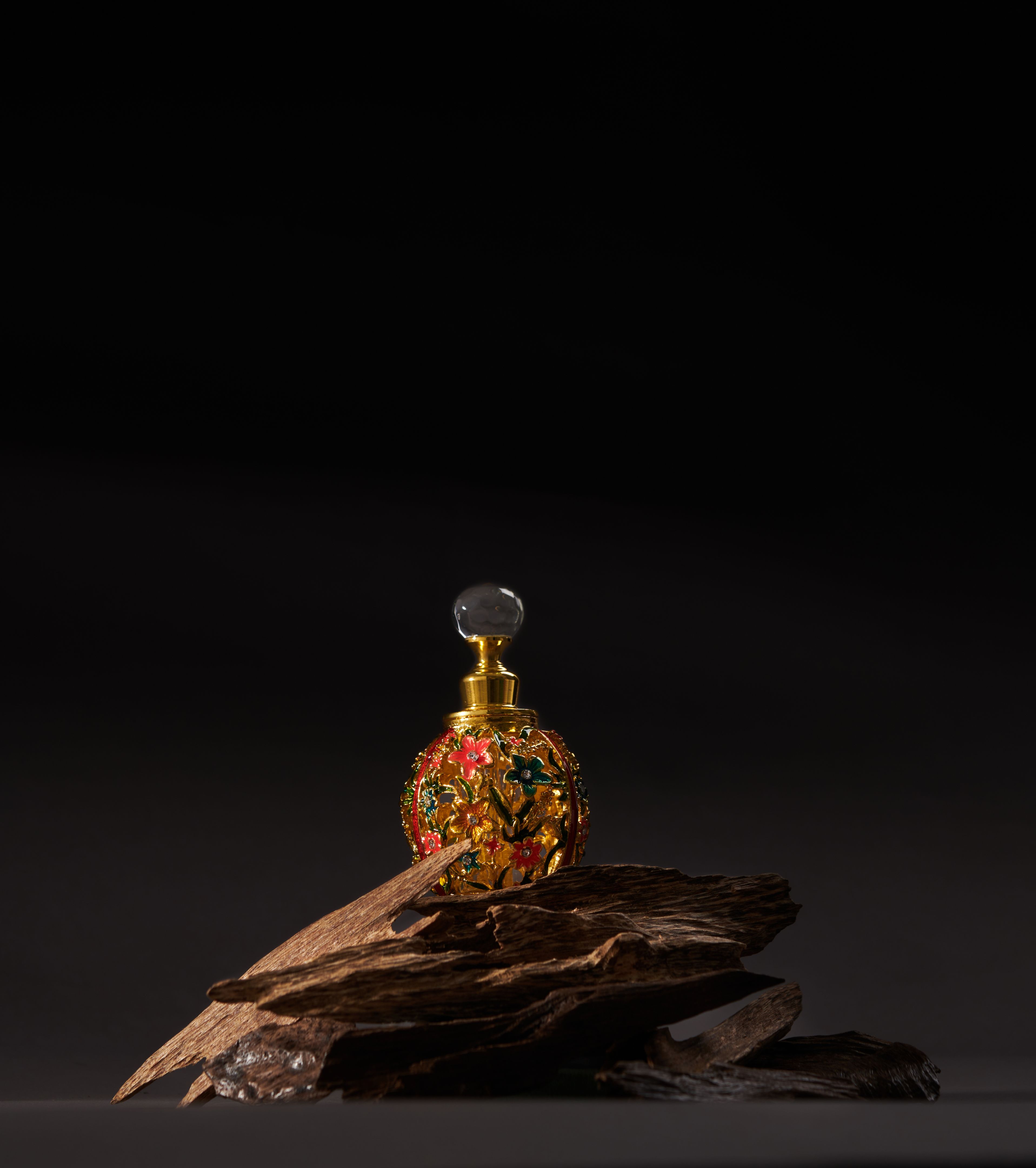 A bottle of agarwood perfume with pieces of agarwood on a dark background.