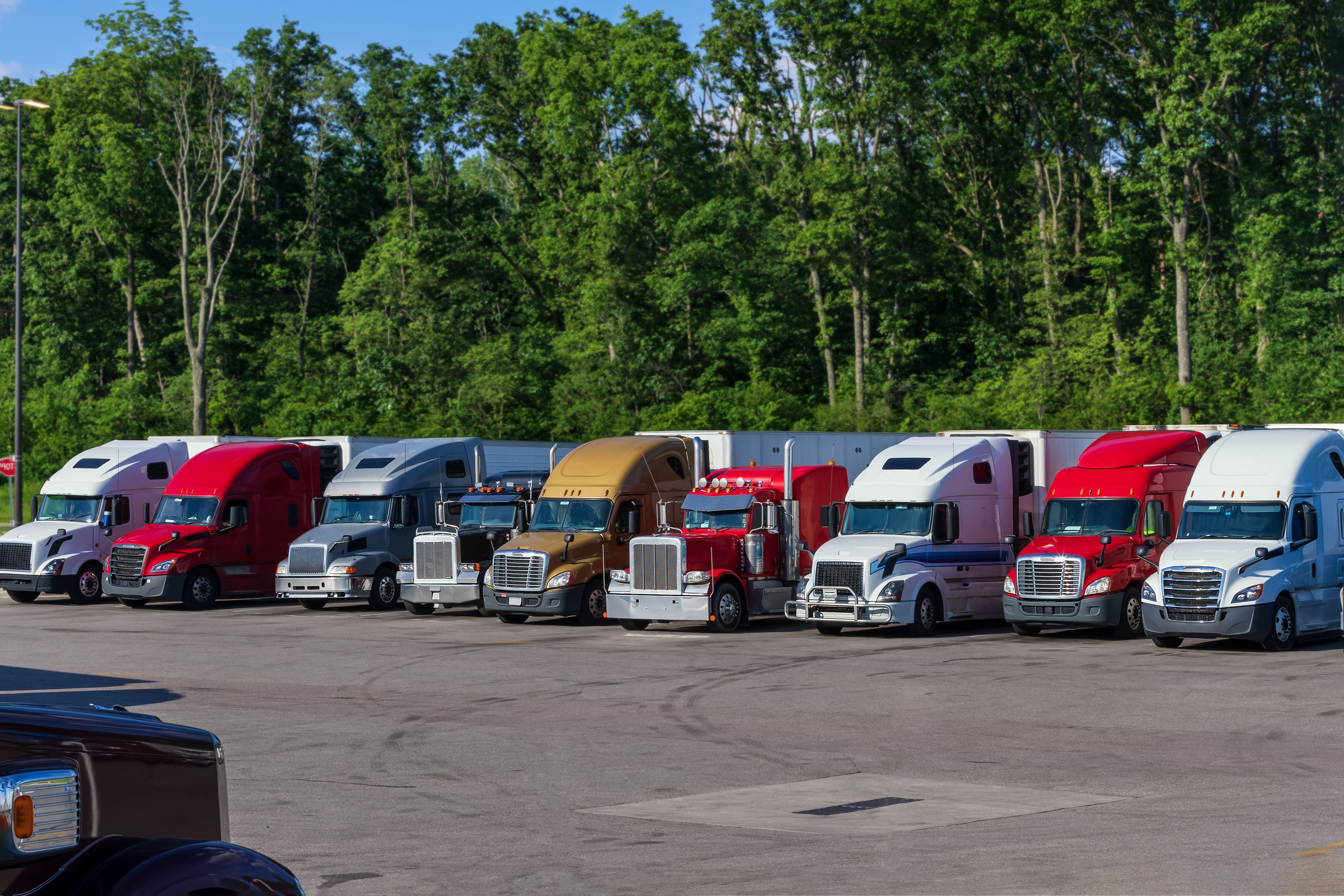Different makes and models industrial grade professional big rigs semi trucks standing in row on the truck stop parking lot.