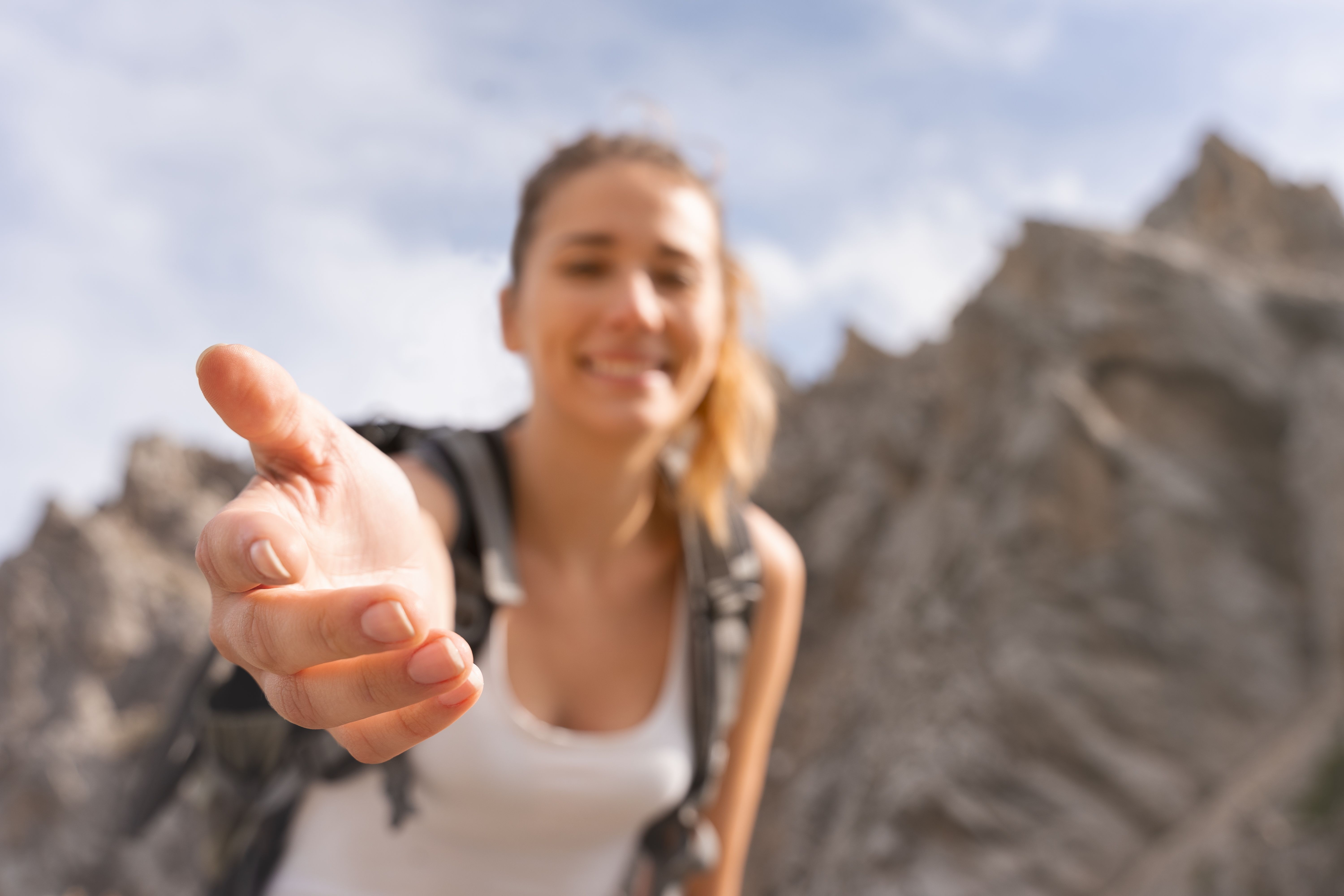 young man on top of the mountain, extending his hand to help you reach the summit