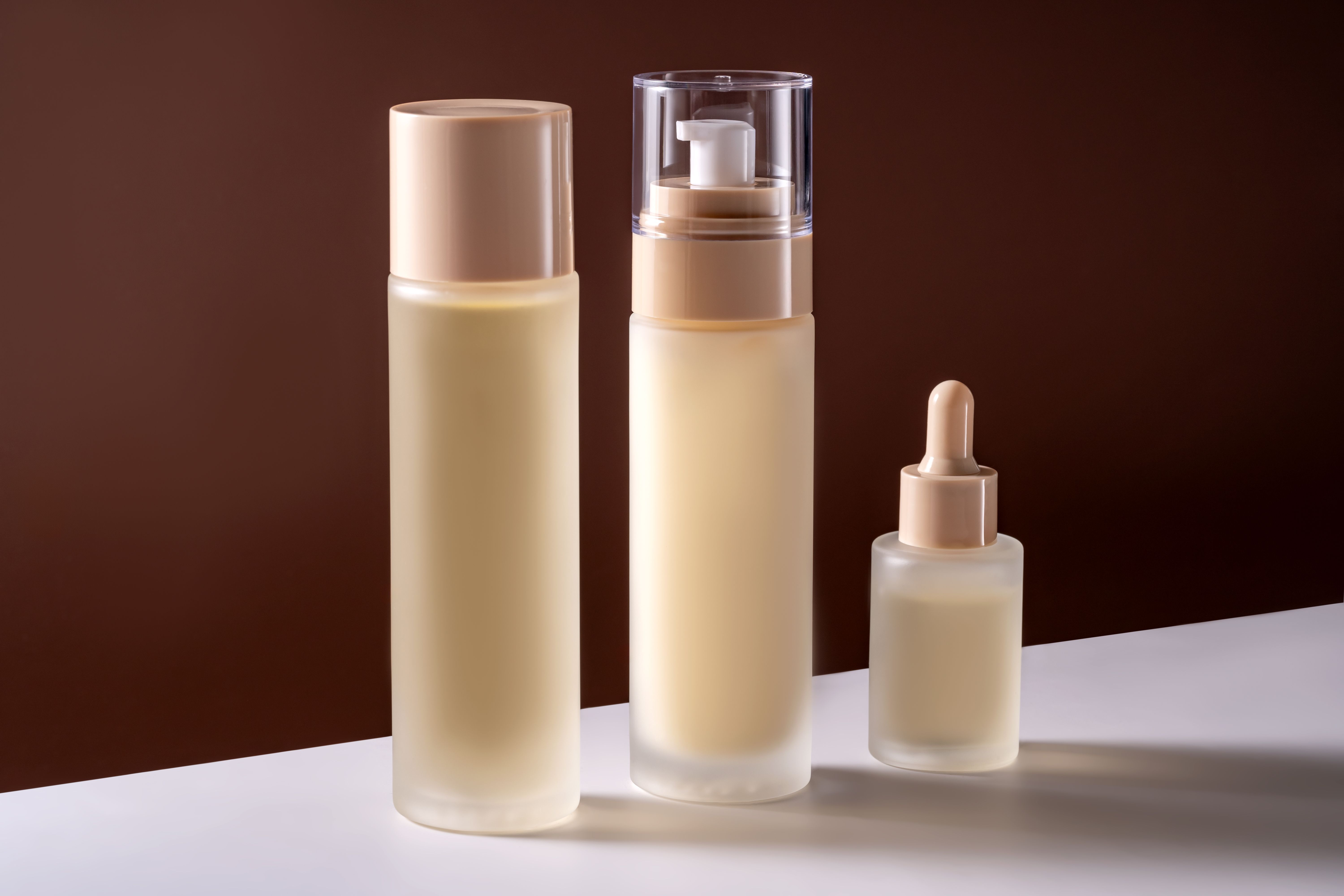 Set of beauty products in glass matte bottles on white table on brown background. Skin care set for daily routine. Mockup for designers. Unbranded package